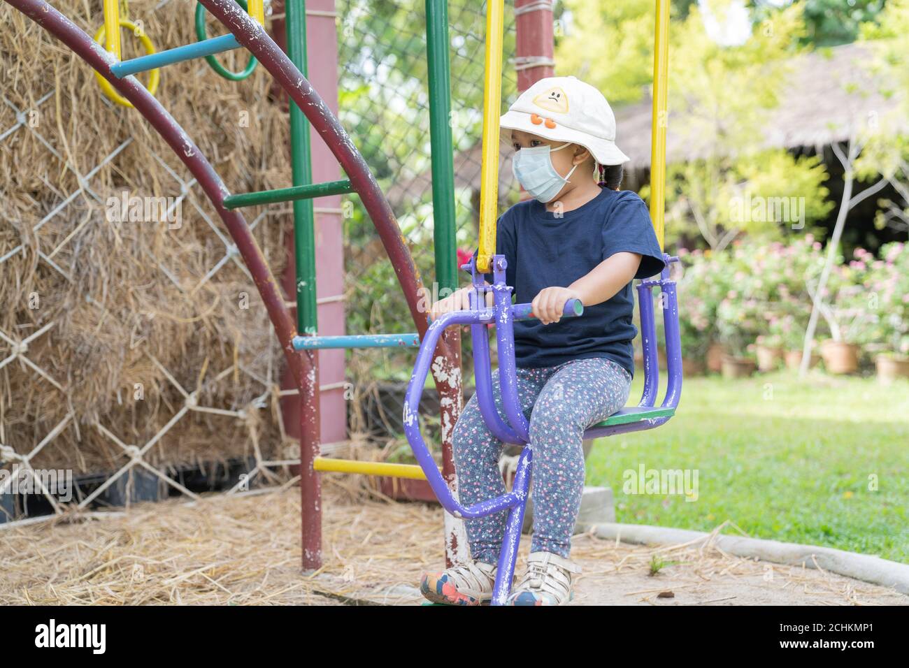 Asiatische Mädchen Kind trägt chirurgische Maske, um die Ausbreitung von Erkältung und Grippe und Viren zu verhindern. Sie haben Spaß und spielen Schaukelpferd im Freien pla Stockfoto