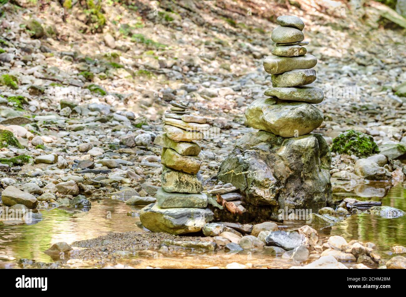 Rock Balancing. Zwei Stapel gestapelter Felsen in einem Flussbett. Felsen lagen flach aufeinander zu großer Höhe. Ausgewogene Felsen am Bach. Stockfoto