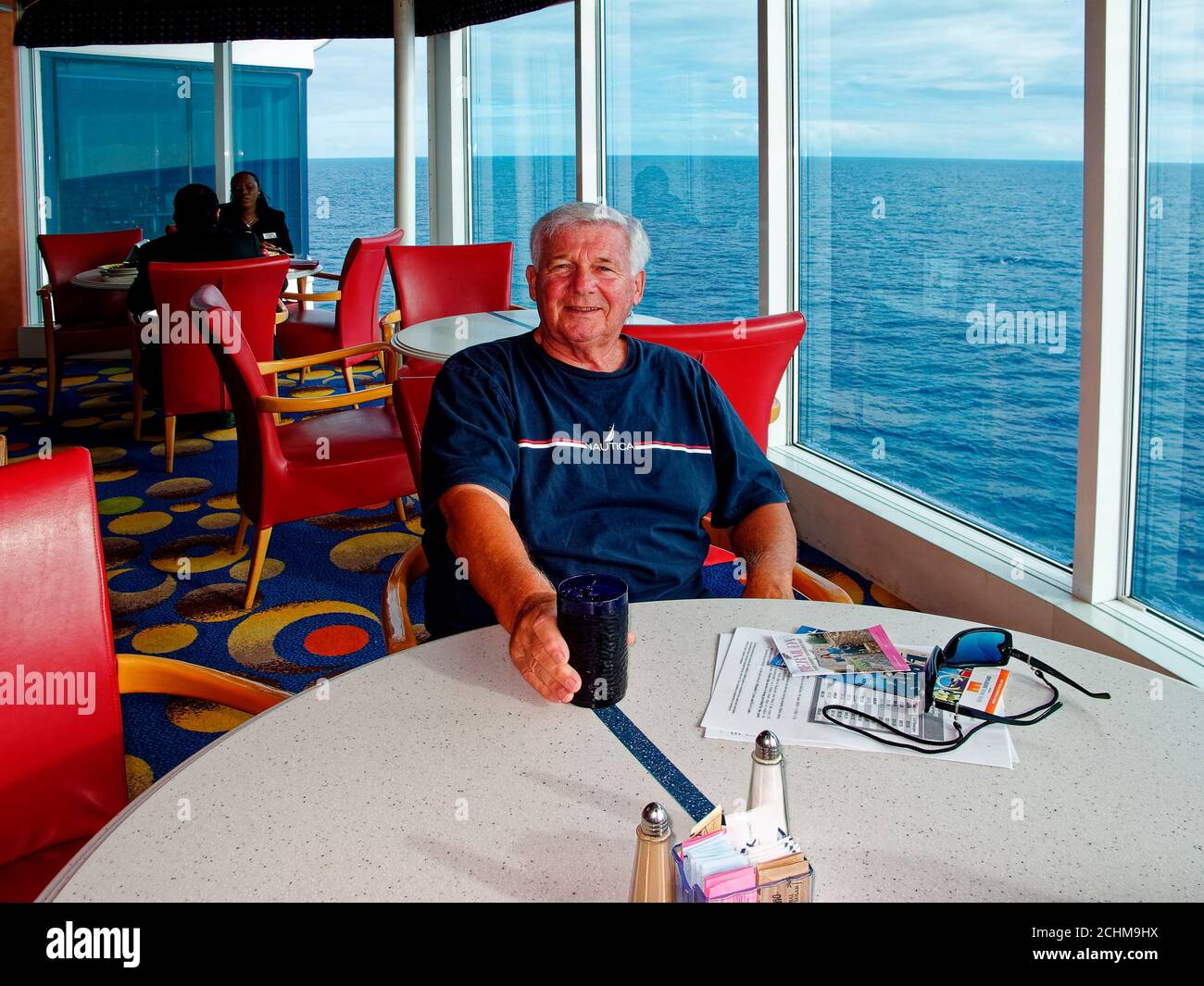 Senior Mann am Tisch, Kreuzfahrtschiff, Fenster, Aqua Ocean, Lesematerial, Entspannung, Reisen, Urlaub, MR Stockfoto