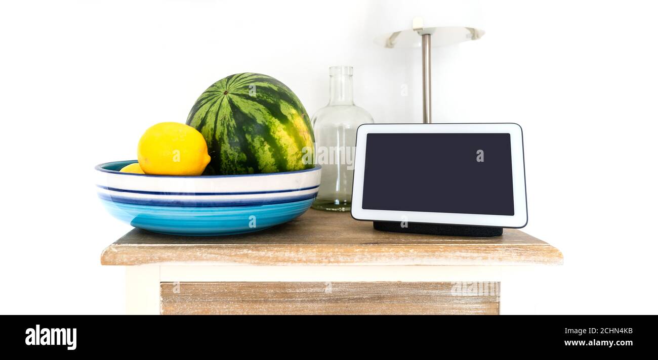 Smart Display und Smart Speaker auf Küchenregal mit Wasser Melone und Zitronen in Obstschale Stockfoto