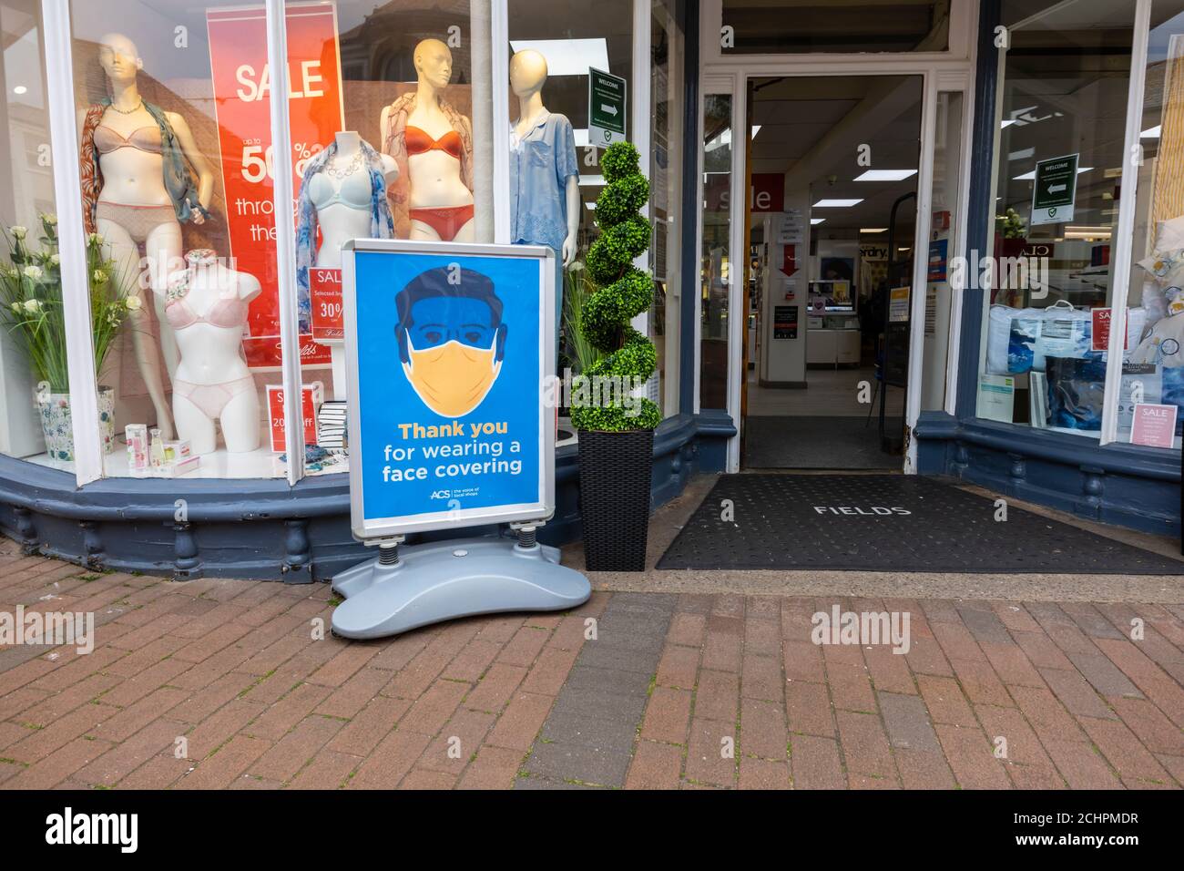 Straßenschild vor dem Eingang des Ladens mit der Aufforderung, dass Kunden beim Betreten eine Gesichtsabdeckung tragen. Sidmouth, eine Küstenstadt in Devon, Südküste Englands Stockfoto