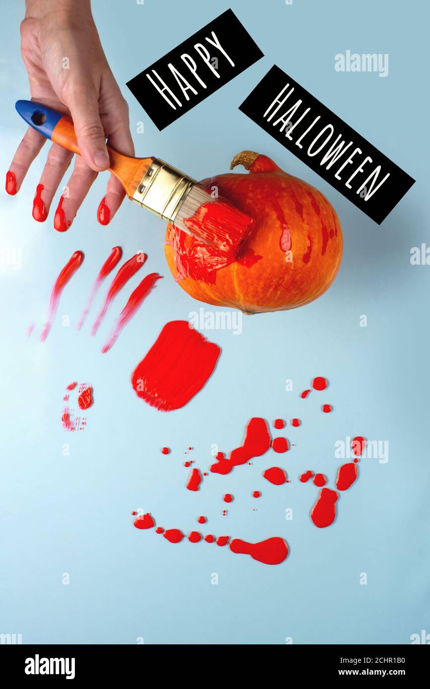 Die Hand mit dem Pinsel malt den Kürbis rot, wie Blut. In der Nähe von Flecken, Tropfen, Spritzer. Halloween-Konzept Stockfoto