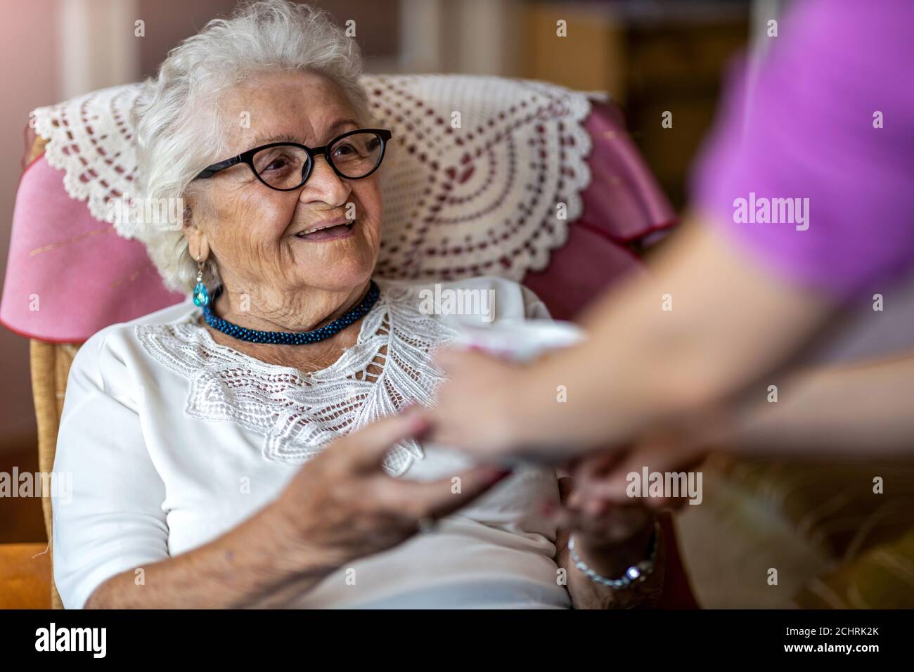 Hilfreiche häusliche Krankenschwester gibt einer älteren Frau eine Tasse Von heißem Tee Stockfoto