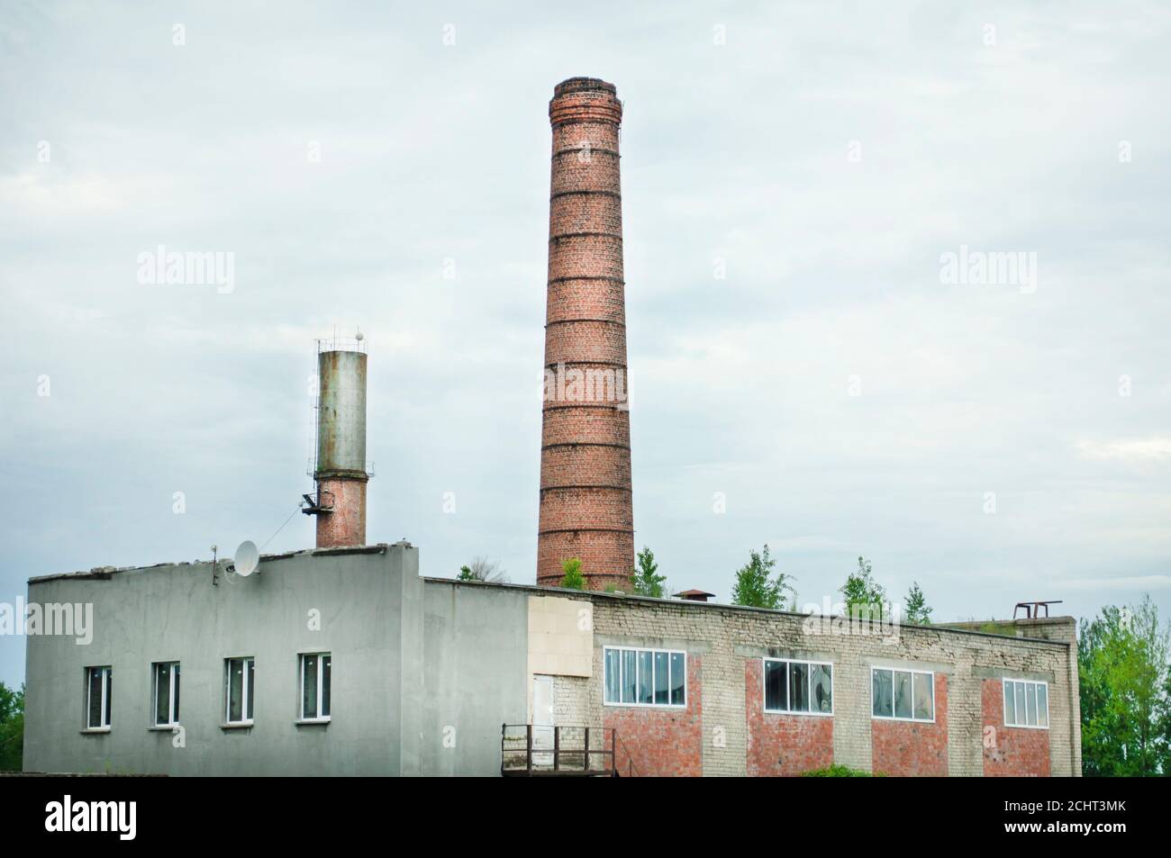 Altes Fabrikgebäude, alte Ziegelrohre aus dem Kesselraum, junge Bäume auf dem Dach, aber mit Fiberglas-Fenstern Stockfoto