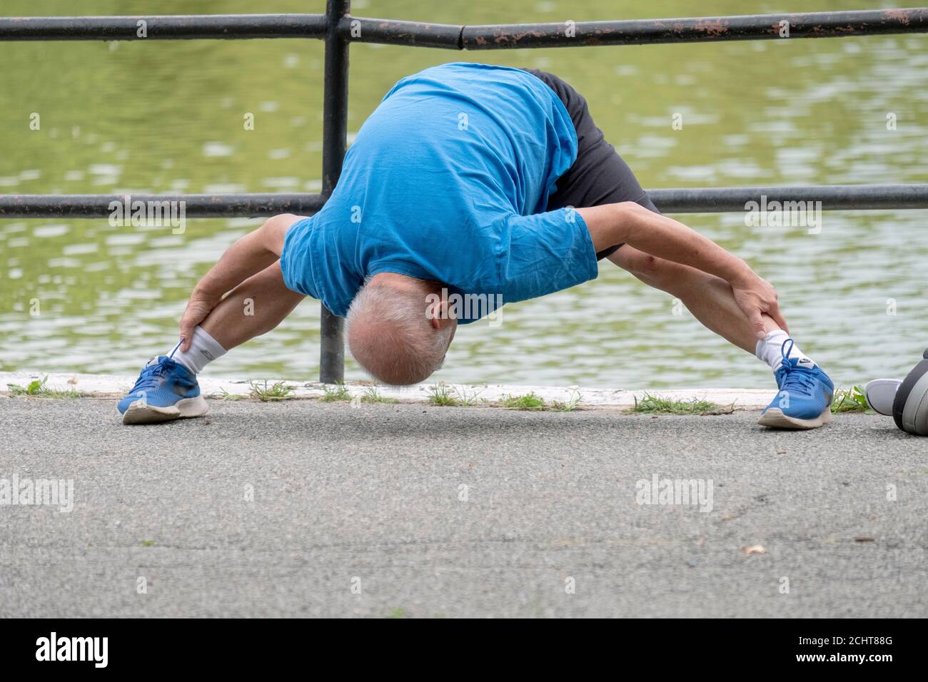 Ein flink flexibler Senior tut etwas extremes Stretching, während er sich für einen Übungsspaziergang aufwärmt. In einem Park in Queens, New York City. Stockfoto