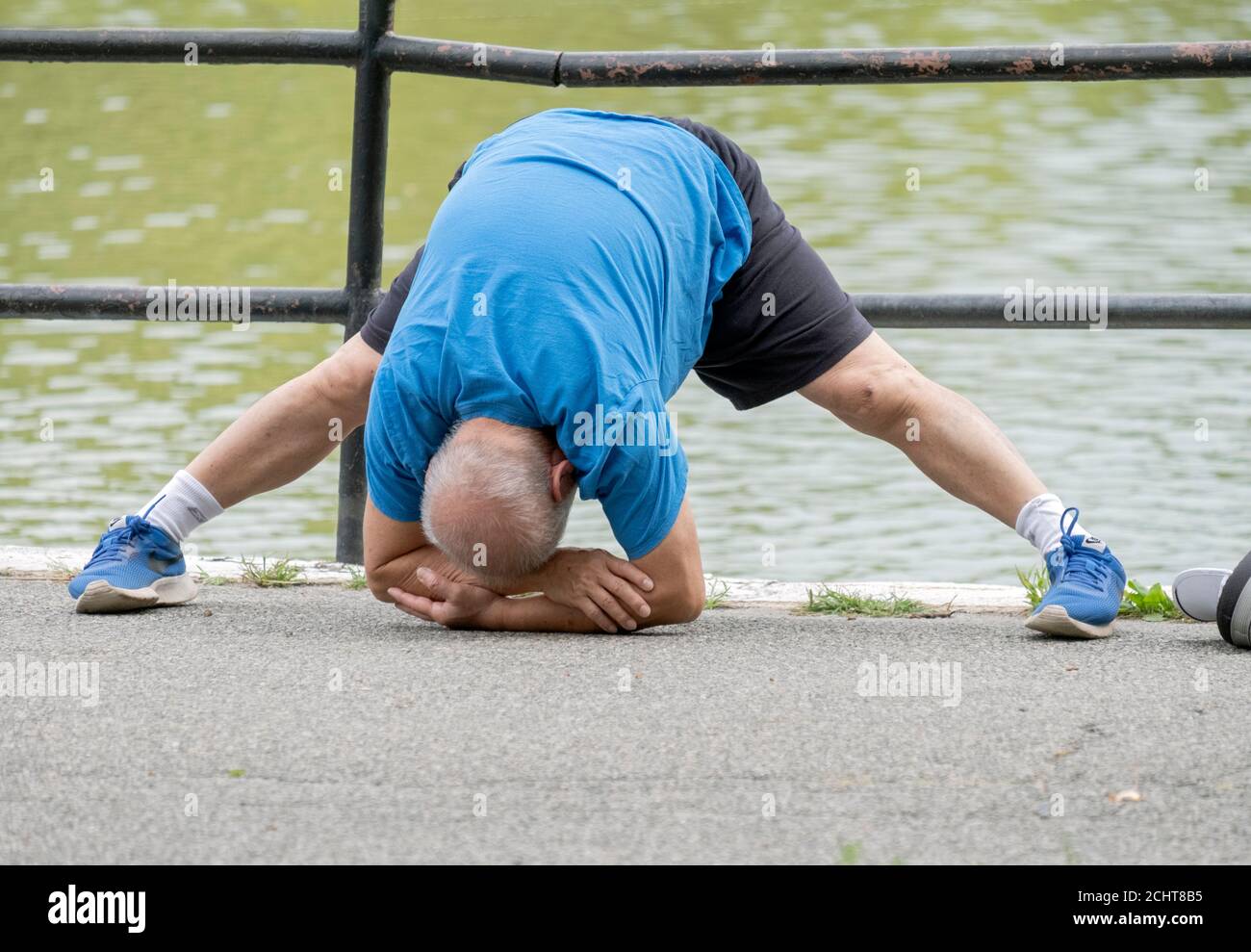 Ein flink flexibler Senior tut etwas extremes Stretching, während er sich für einen Übungsspaziergang aufwärmt. In einem Park in Queens, New York City. Stockfoto