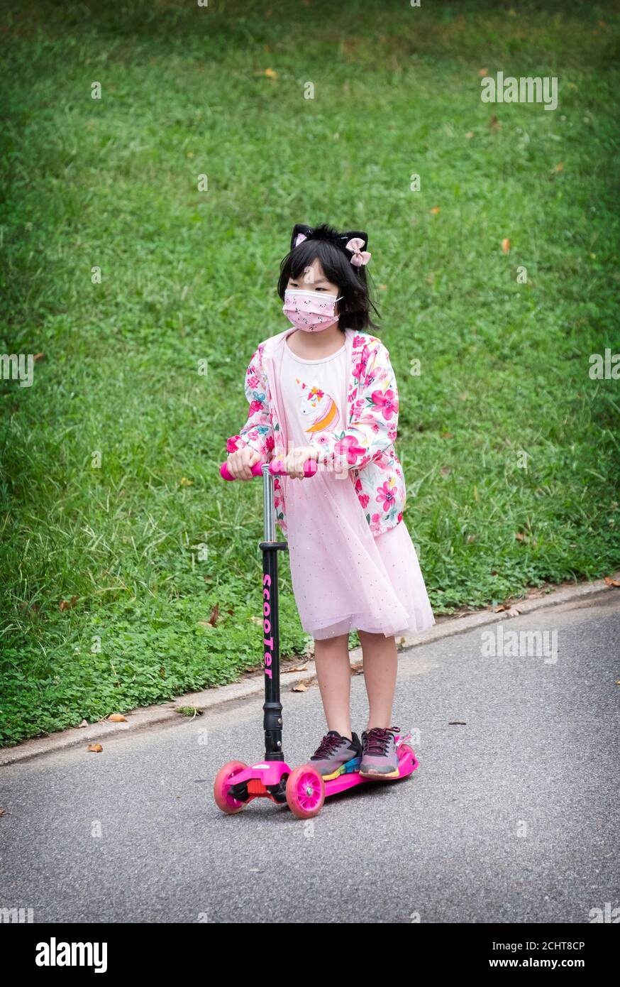 Ein extrem süßes asiatisch-amerikanisches Mädchen, das in Rosa gekleidet ist, fährt ihren Allrad-Roller in einem Park in Queens, New York City. Stockfoto