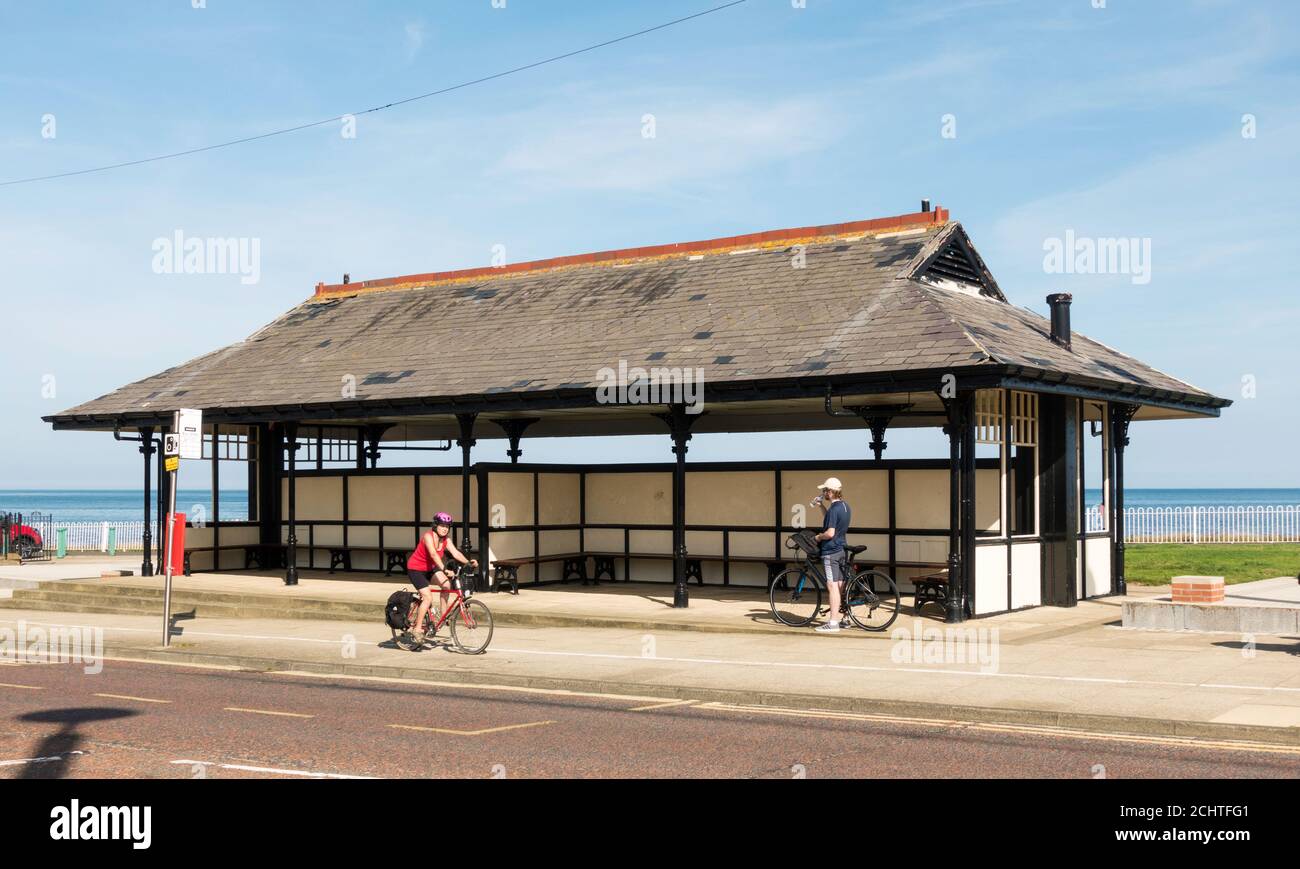 Radfahrerin, die am Anfang des 20. Jahrhunderts vorbeifahrenden Tram Shelter, jetzt Seaside Shelter und Bushaltestelle, in Seaburn, Sunderland, England, Großbritannien, vorbeifährt Stockfoto