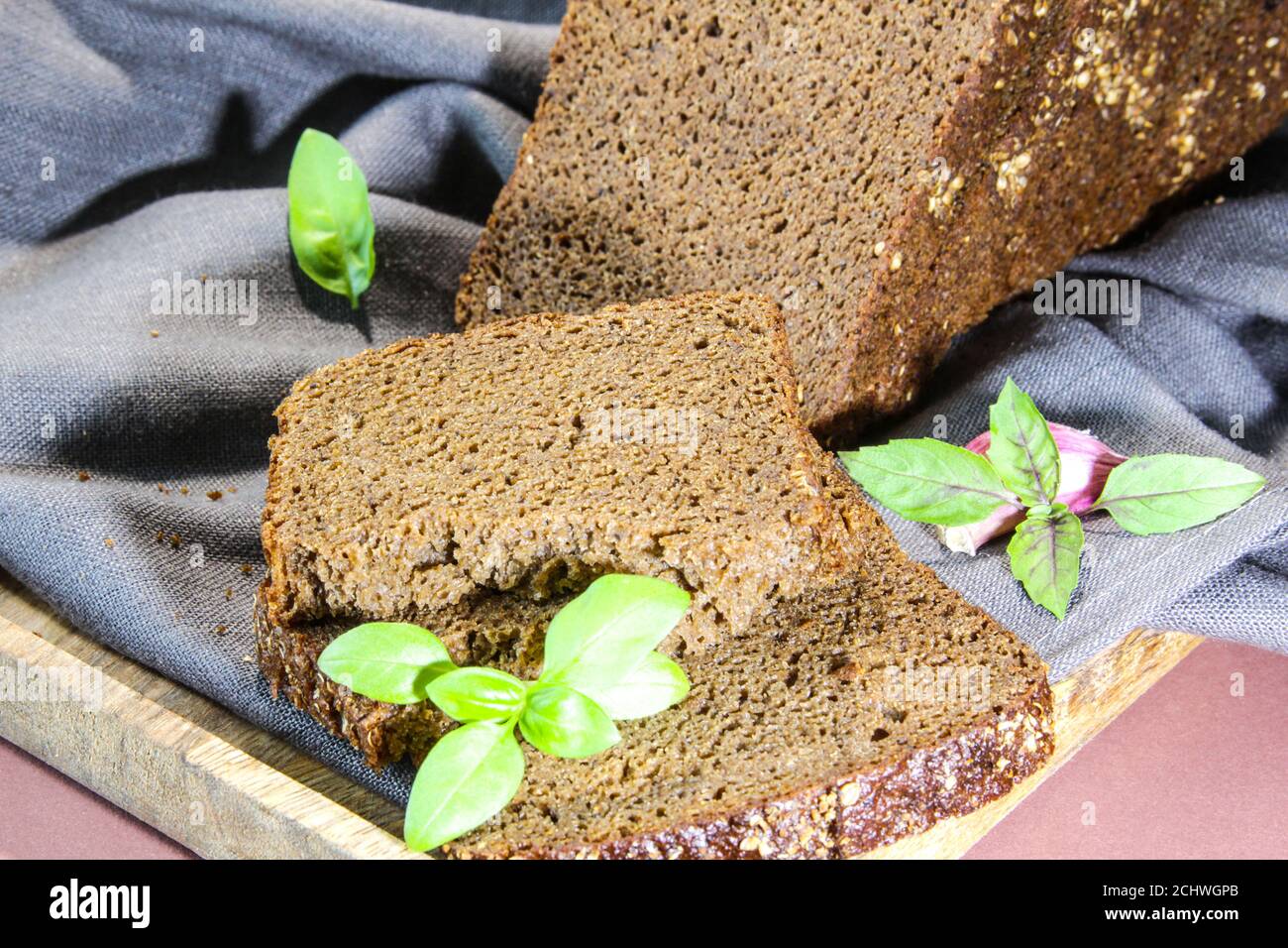 Geschnittenes Roggenbrot mit Blattbasil auf Schneidebrett. Vollkorn Roggenbrot mit Samen Stockfoto