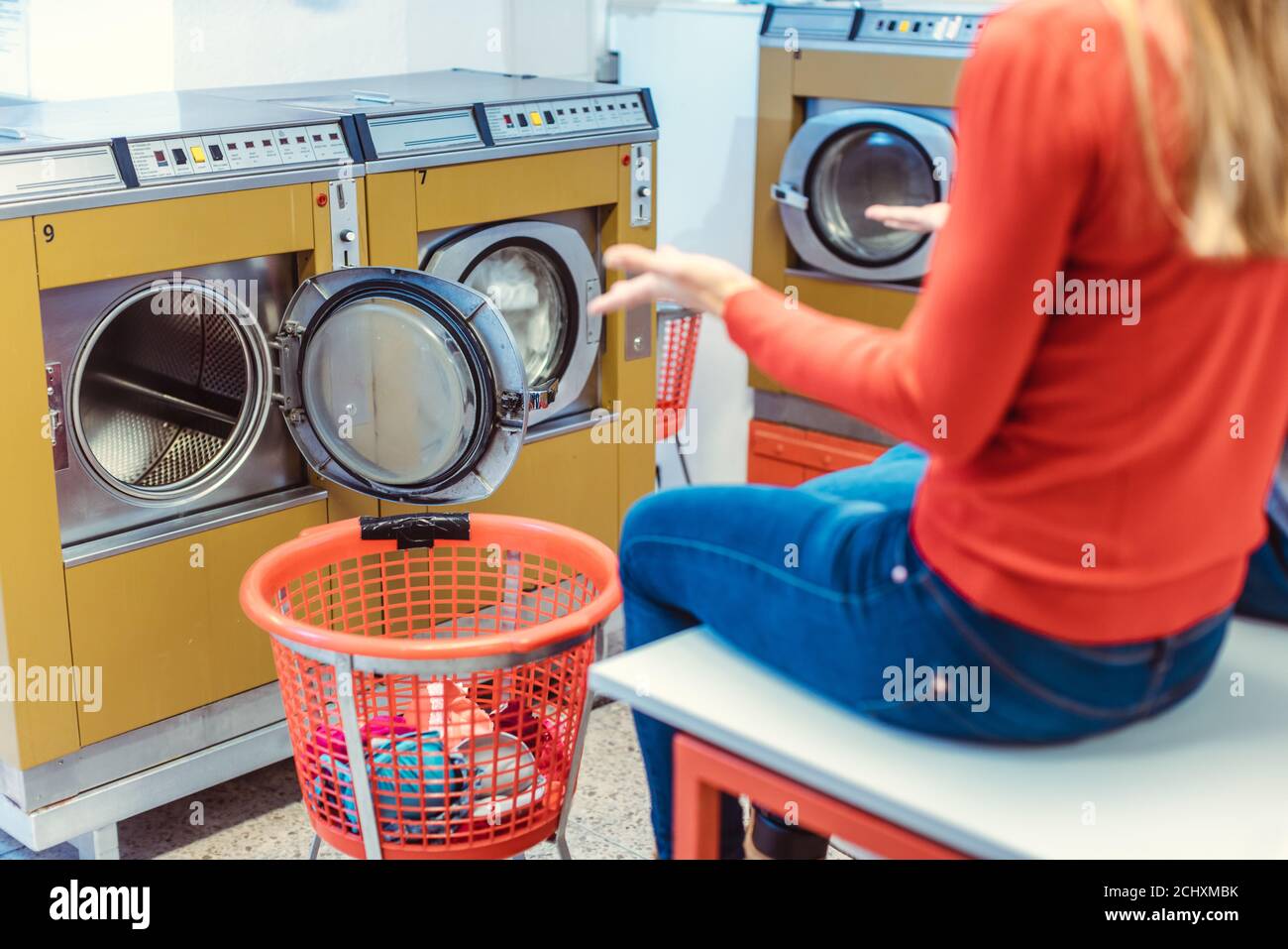 Frau sitzt erstaunt vor der Waschmaschine im Waschsalon Stockfoto