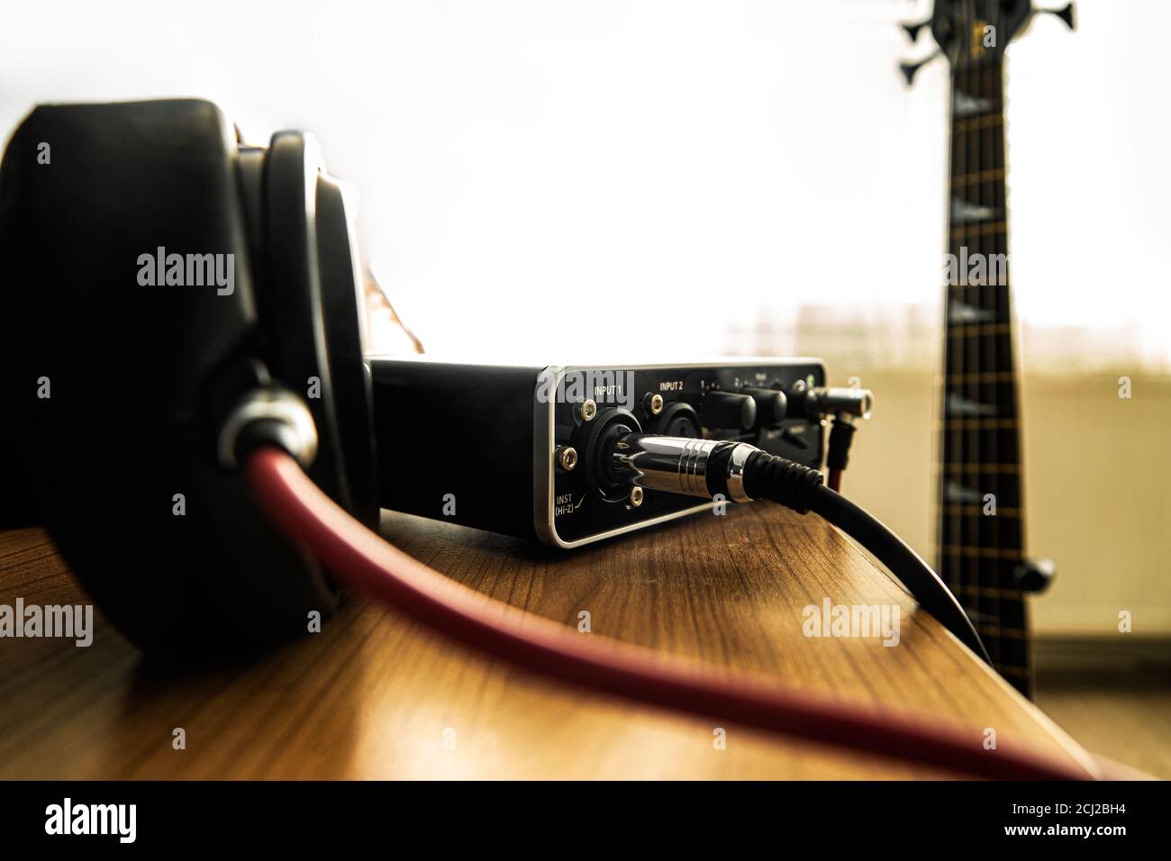 Kopfhörer und Soundkarte auf dem Tisch und eine Bassgitarre auf dem Hintergrund. Stockfoto