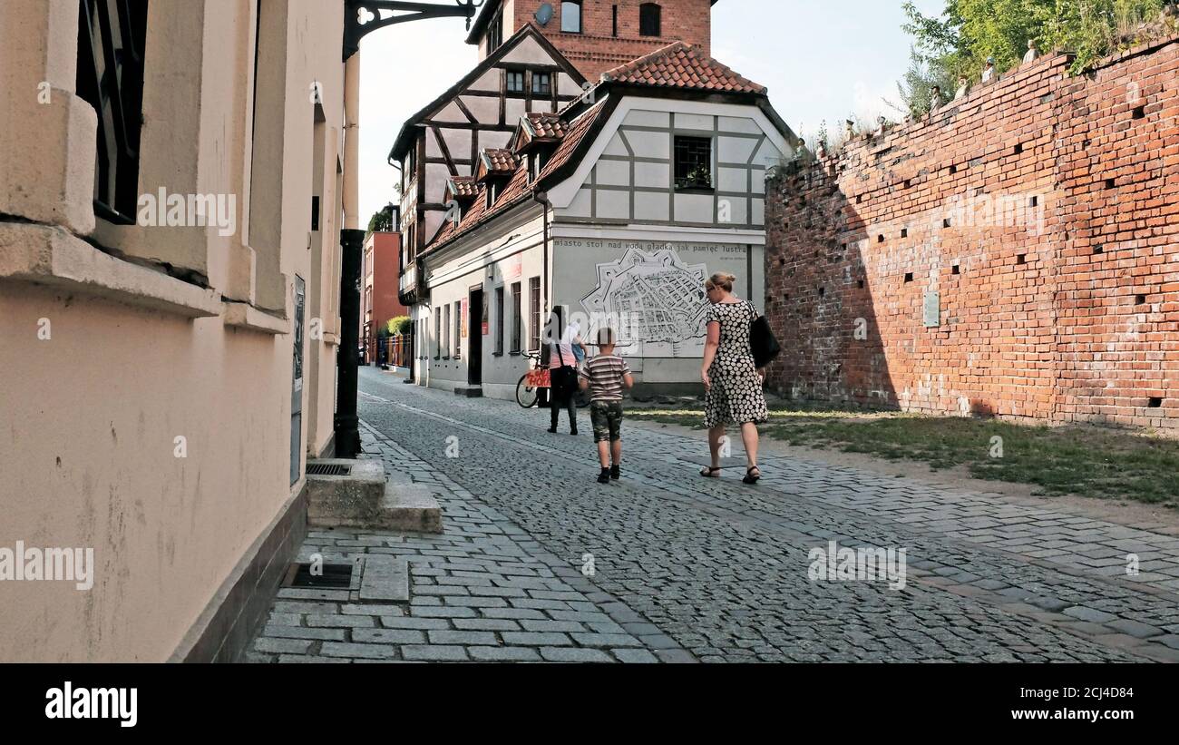 Drei Personen gehen auf einer gepflasterten Straße in der Altstadt von Torun, Polen. Stockfoto