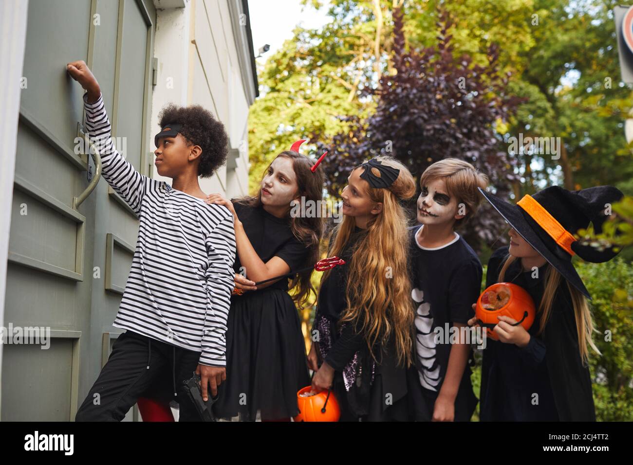 Seitenansicht bei multi-ethnischen Gruppe von Kindern tragen Halloween-Kostüme Klingeln Türklingel während Trick oder Behandlung zusammen, kopieren Raum Stockfoto