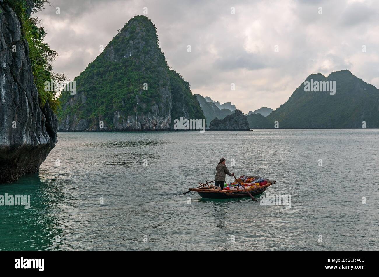 Vietnamesische Verkäuferin auf traditionellem Boot zwischen dem Karst von Halong Bay, Südchinesisches Meer, Nordvietnam. Stockfoto