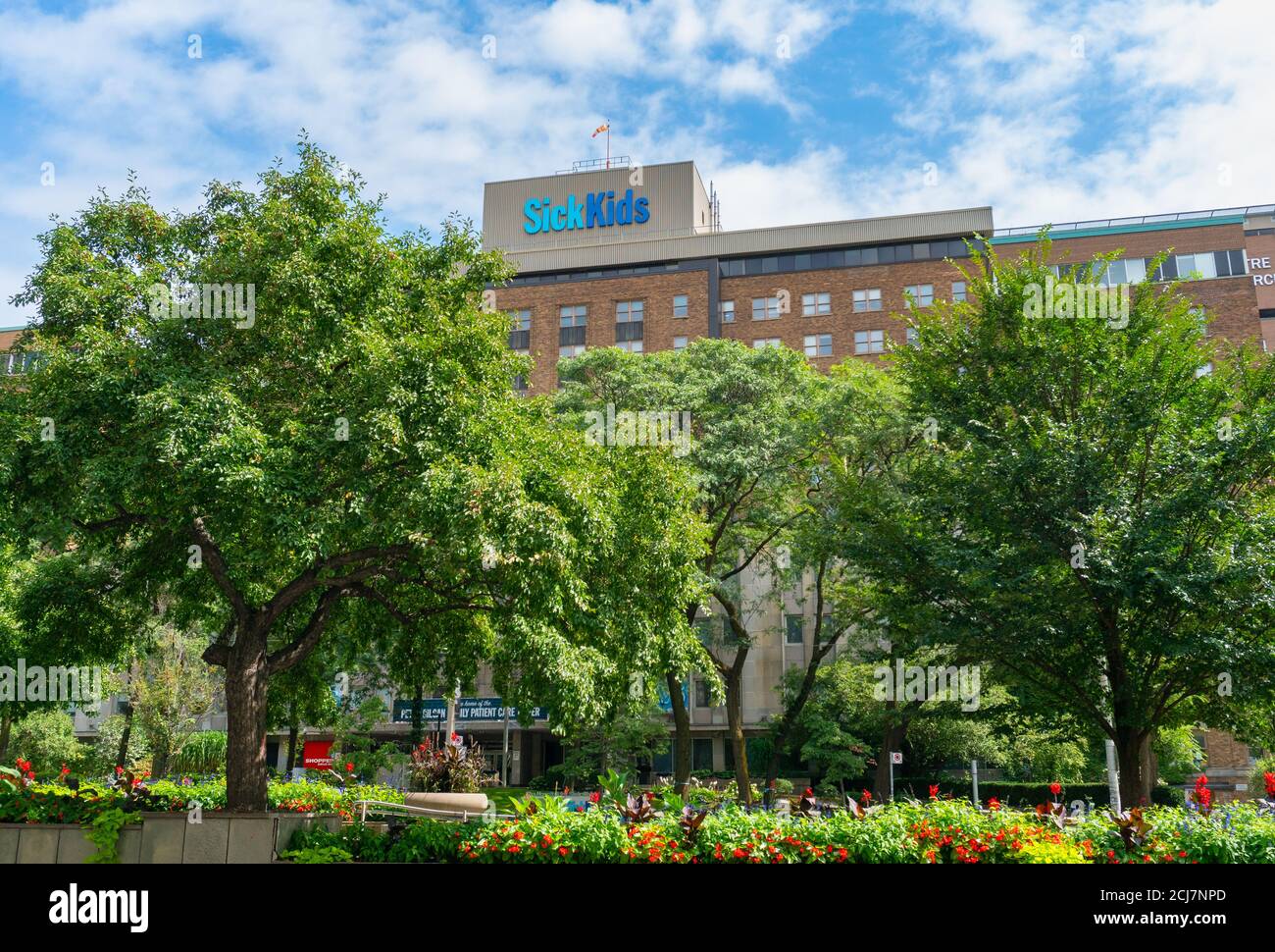 Toronto Sick Kids Hospital Gebäude hinter üppigen Bäumen und Blumenbeeten Unter blauem Himmel mit weißen Wolken Stockfoto