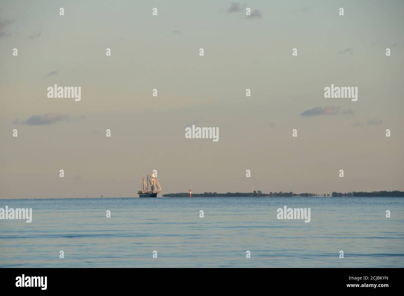 Altes Segelschiff mit vollen Segeln passiert ein weit entferntes Lichthaus, draußen am Horizont. Stockfoto