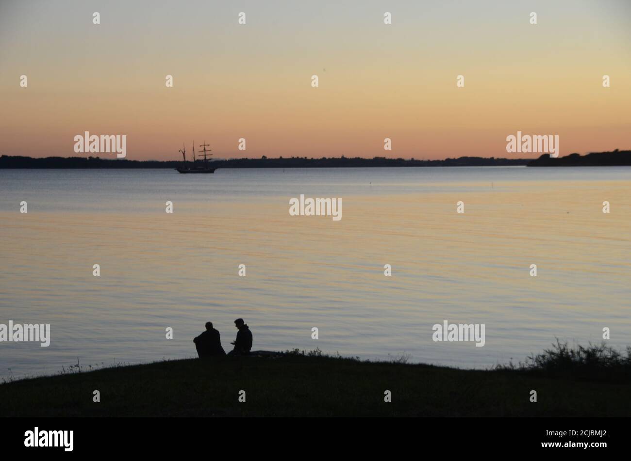 Altes Segelschiff passiert auf dem Meer, während zwei Personen in Silhouette Uhr Stockfoto