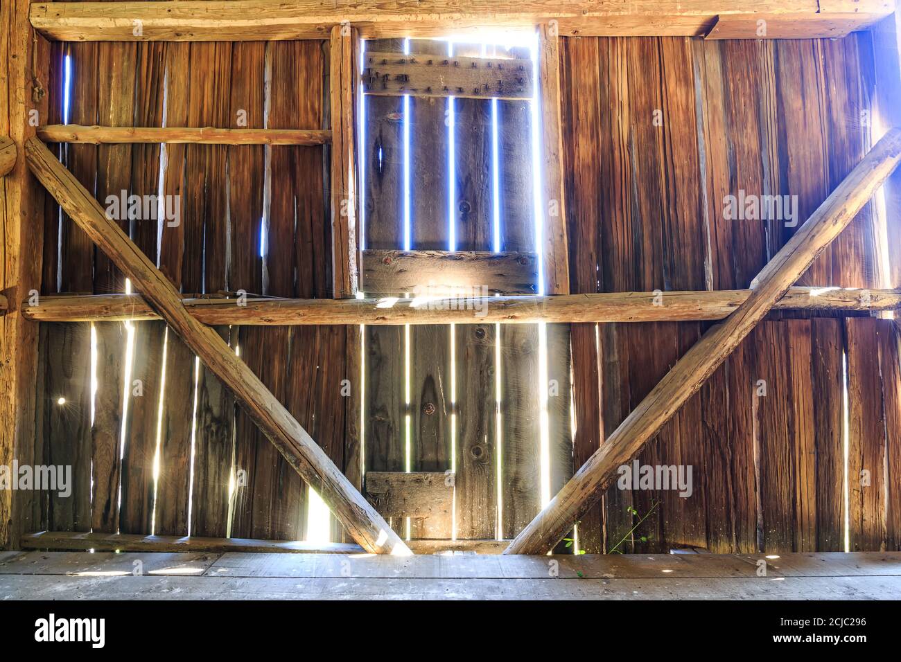 Das Innere einer alten Scheune mit Sonnenlicht, das durch die Bretter strömt. Stockfoto