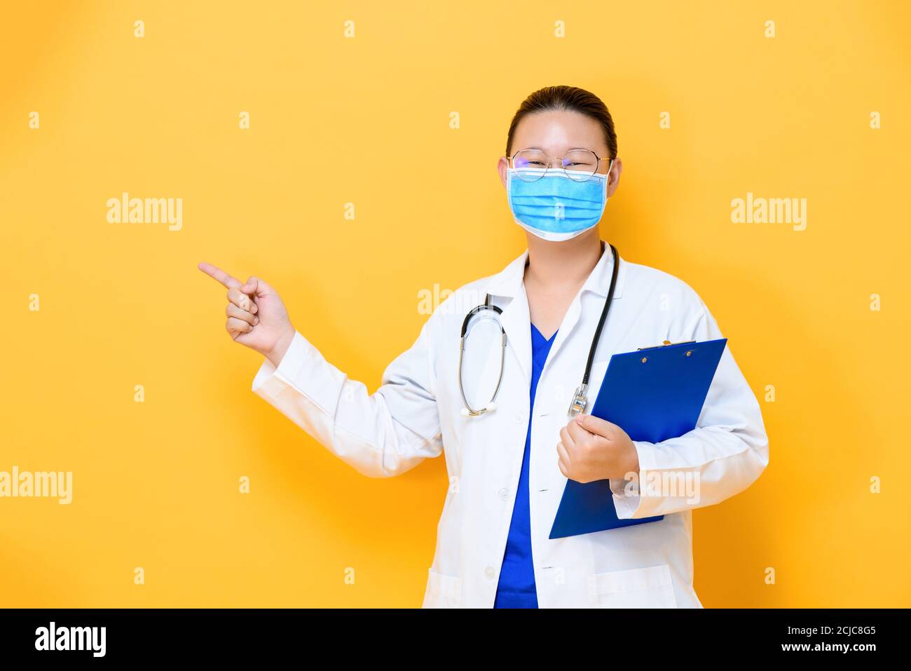 Junge asiatische Frau Arzt trägt medizinische Maske poiting zu leer Abstand beiseite isoliert auf gelbem Hintergrund Stockfoto