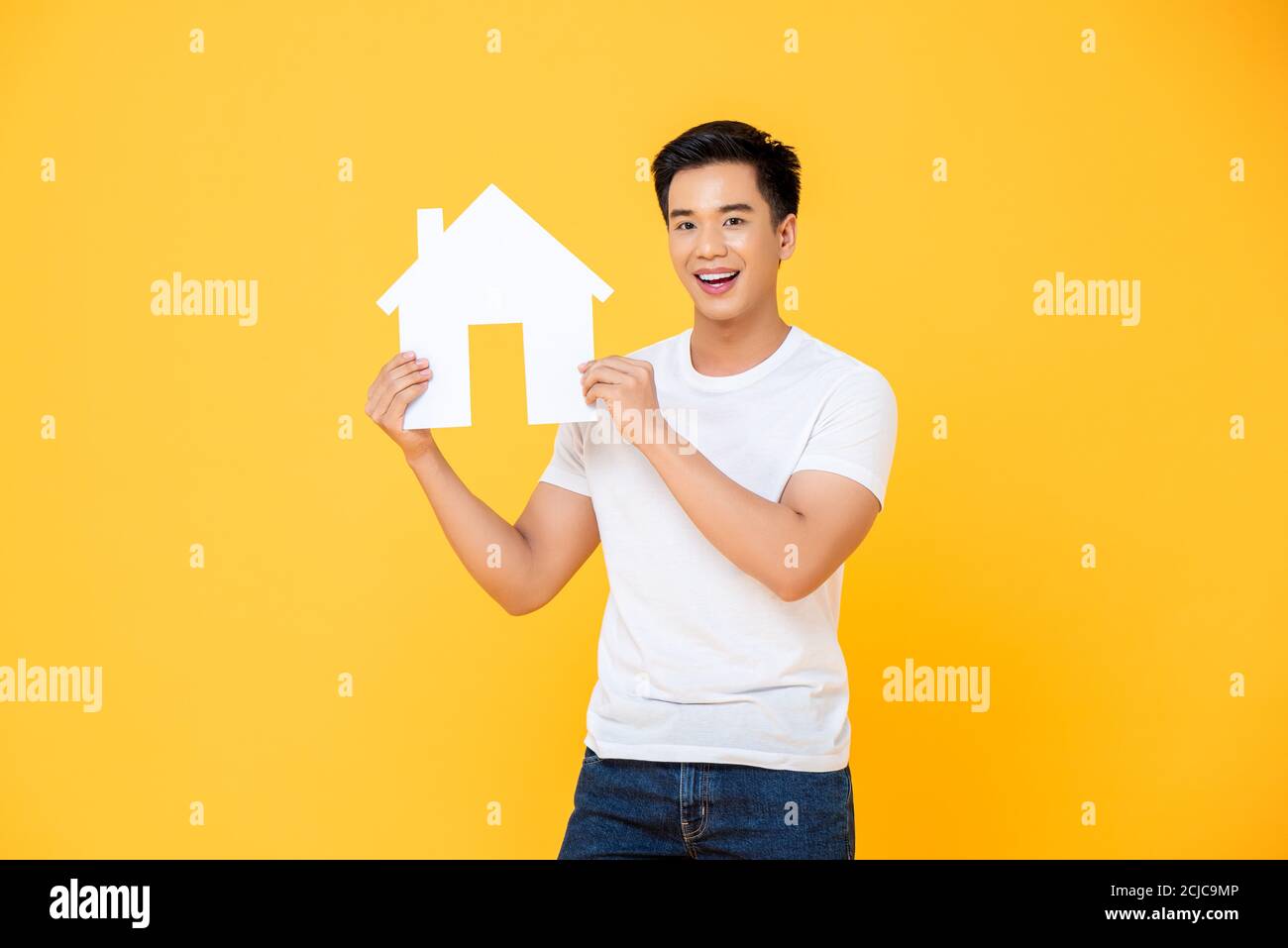 Junge asiatische Mann hält neue Haus Modell Ausschnitt isoliert auf gelbem Hintergrund Stockfoto