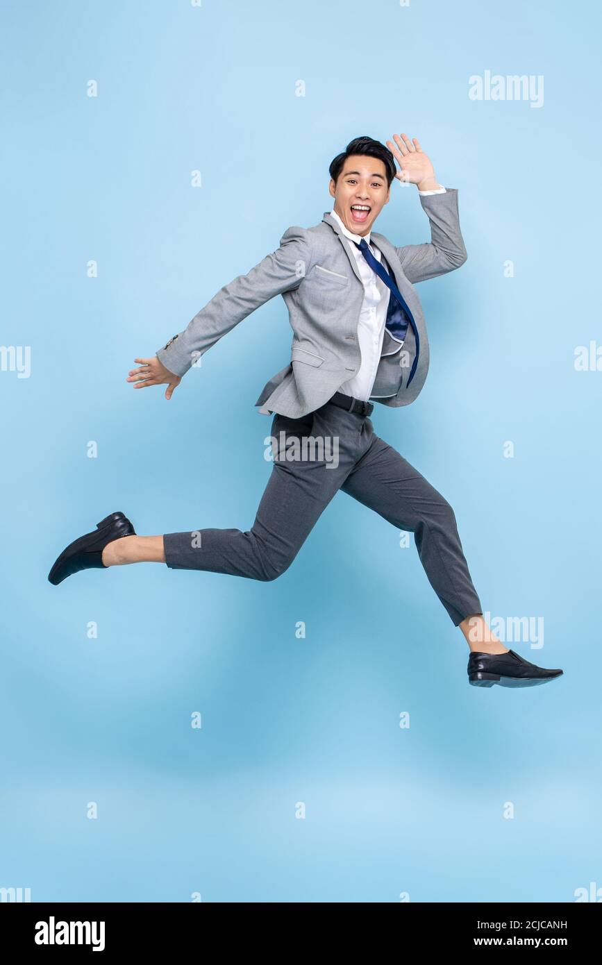 Voller Länge Spaß Porträt von glücklich energisch junge asiatische Geschäftsmann Springen in der Luft isoliert auf Studio blauen Hintergrund Stockfoto