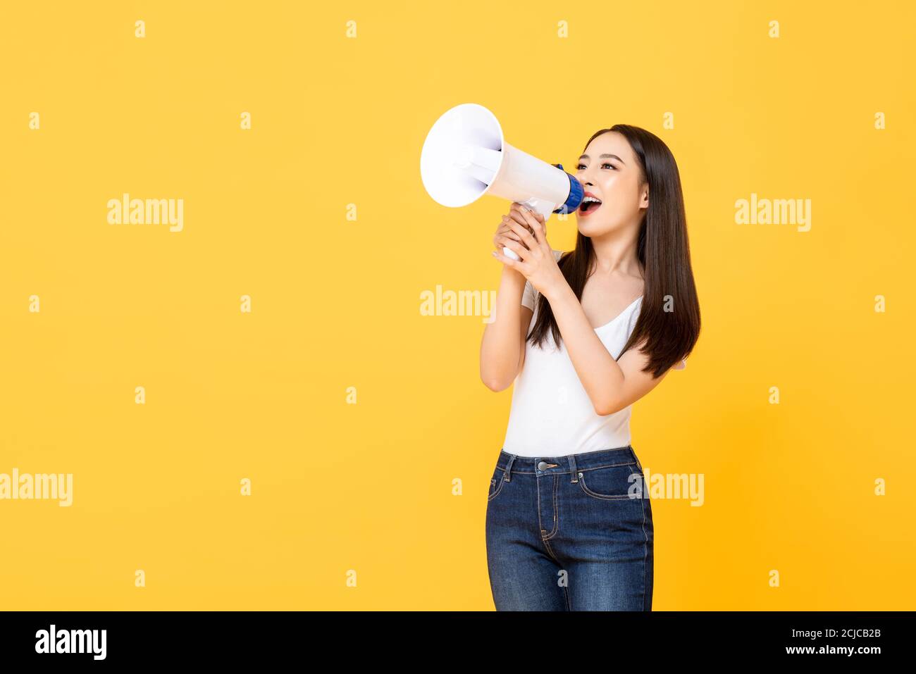 Portrait von lächelnd fröhlich junge hübsche asiatische Frau hält Megaphon Ankündigung in isolierten Studio gelben Hintergrund Stockfoto
