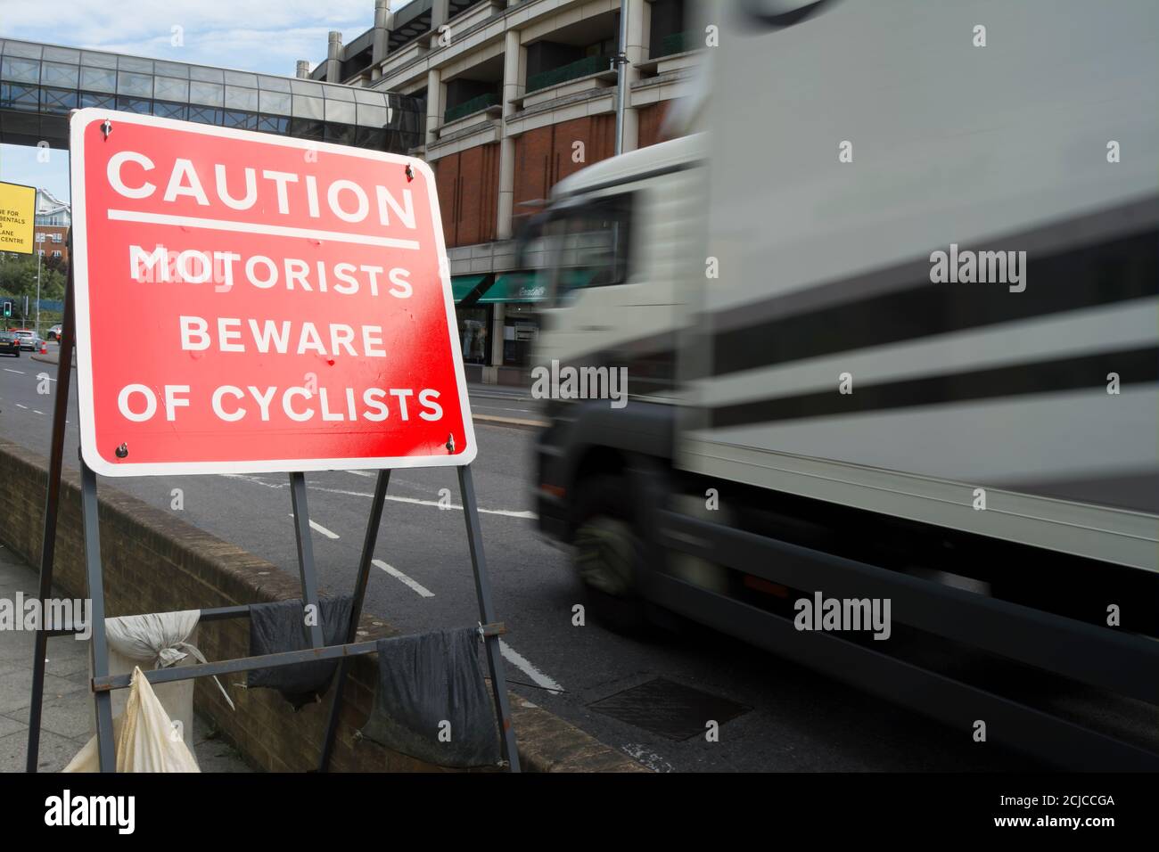 LKW in unscharfer Bewegung gesehen vorbei an einem Autofahrer hüten sich vor Radfahrer Vorsicht Schild, kingston upon thames, surrey, england Stockfoto