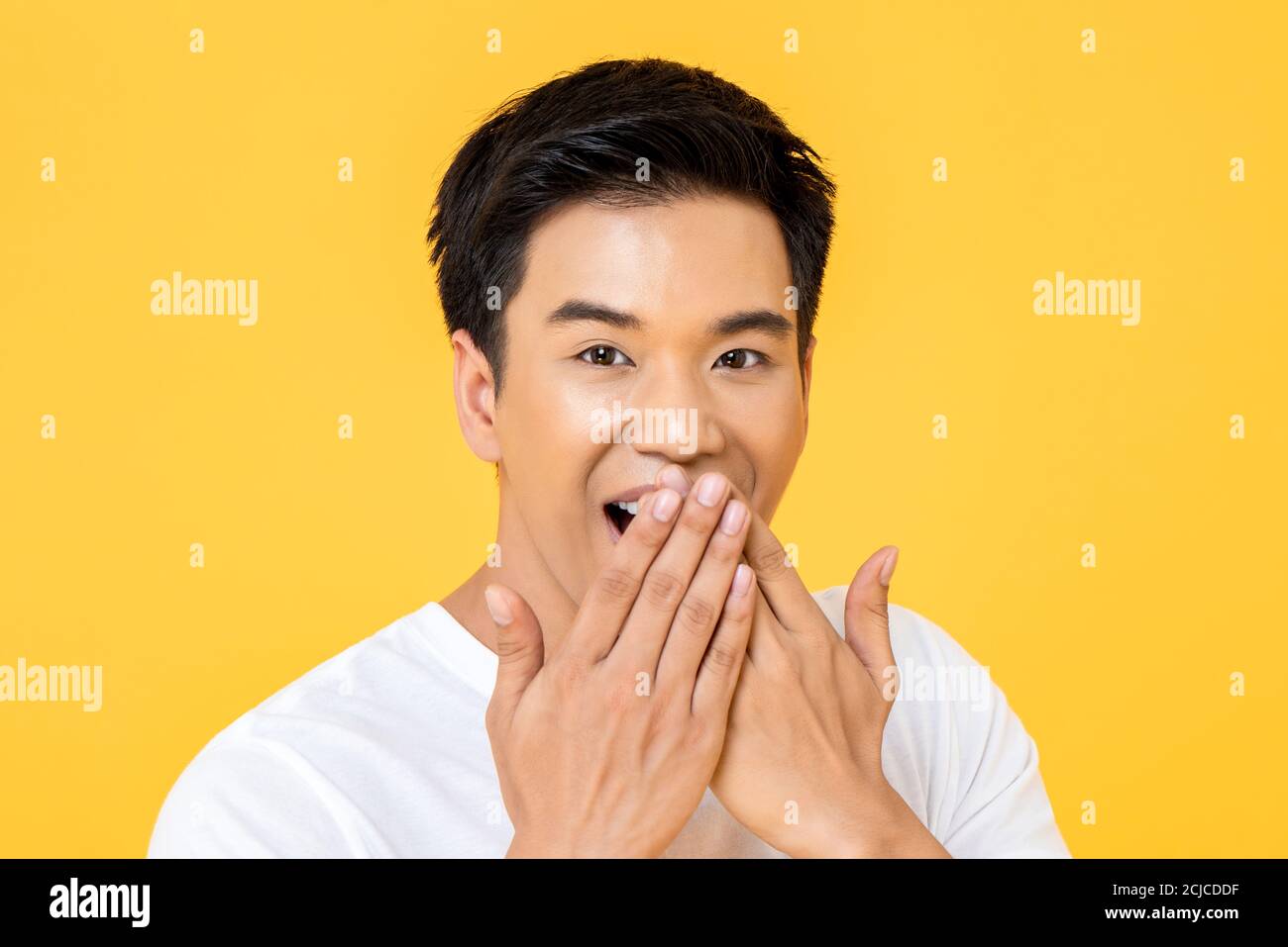 Nahaufnahme Porträt von überrascht jungen asiatischen Mann mit Händen Abdeckung Mund isoliert auf Studio gelben Hintergrund Stockfoto
