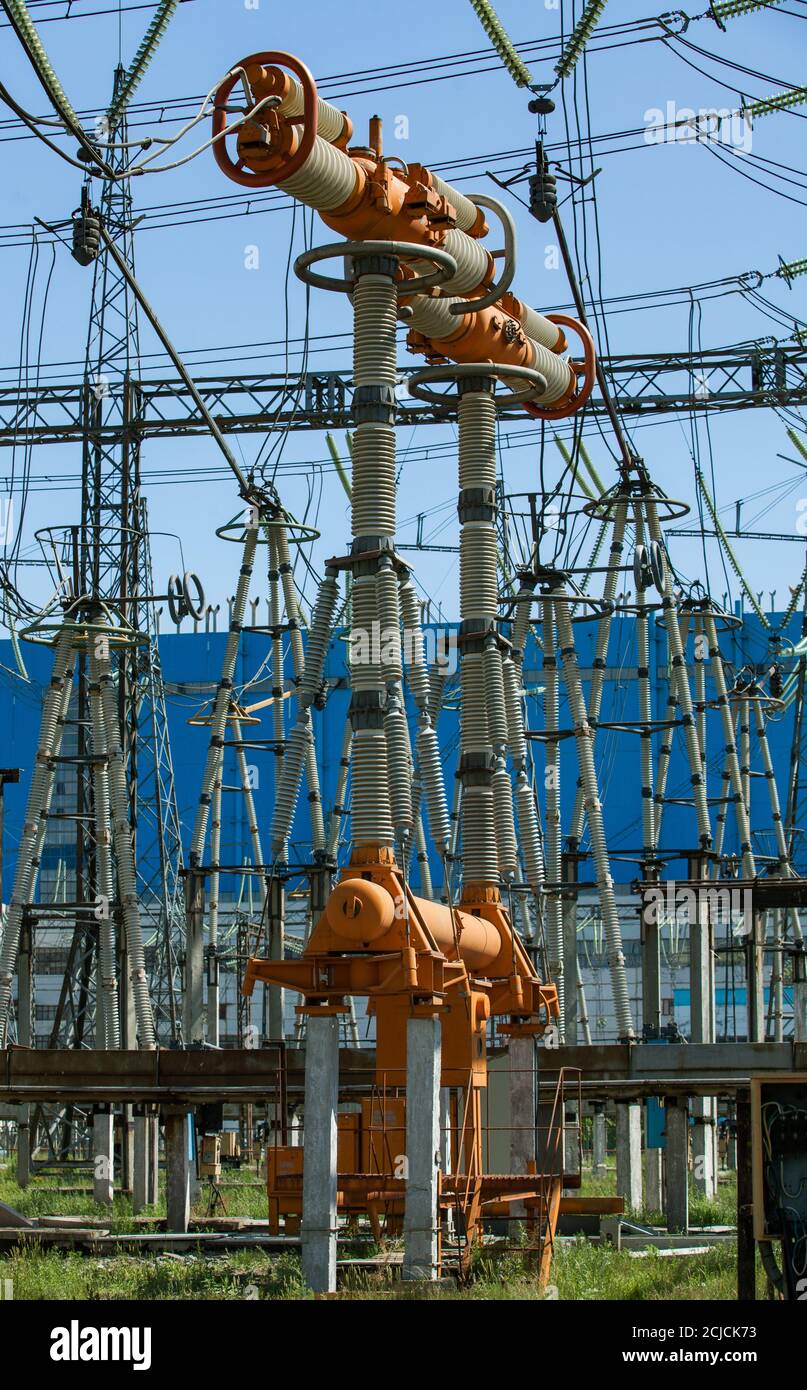 Elektrische Unterstation. Hochspannungsanlagen, elektrische Isolatoren und Schalter auf blauem Fabrikgebäude und blauem Himmel Hintergrund. Stockfoto