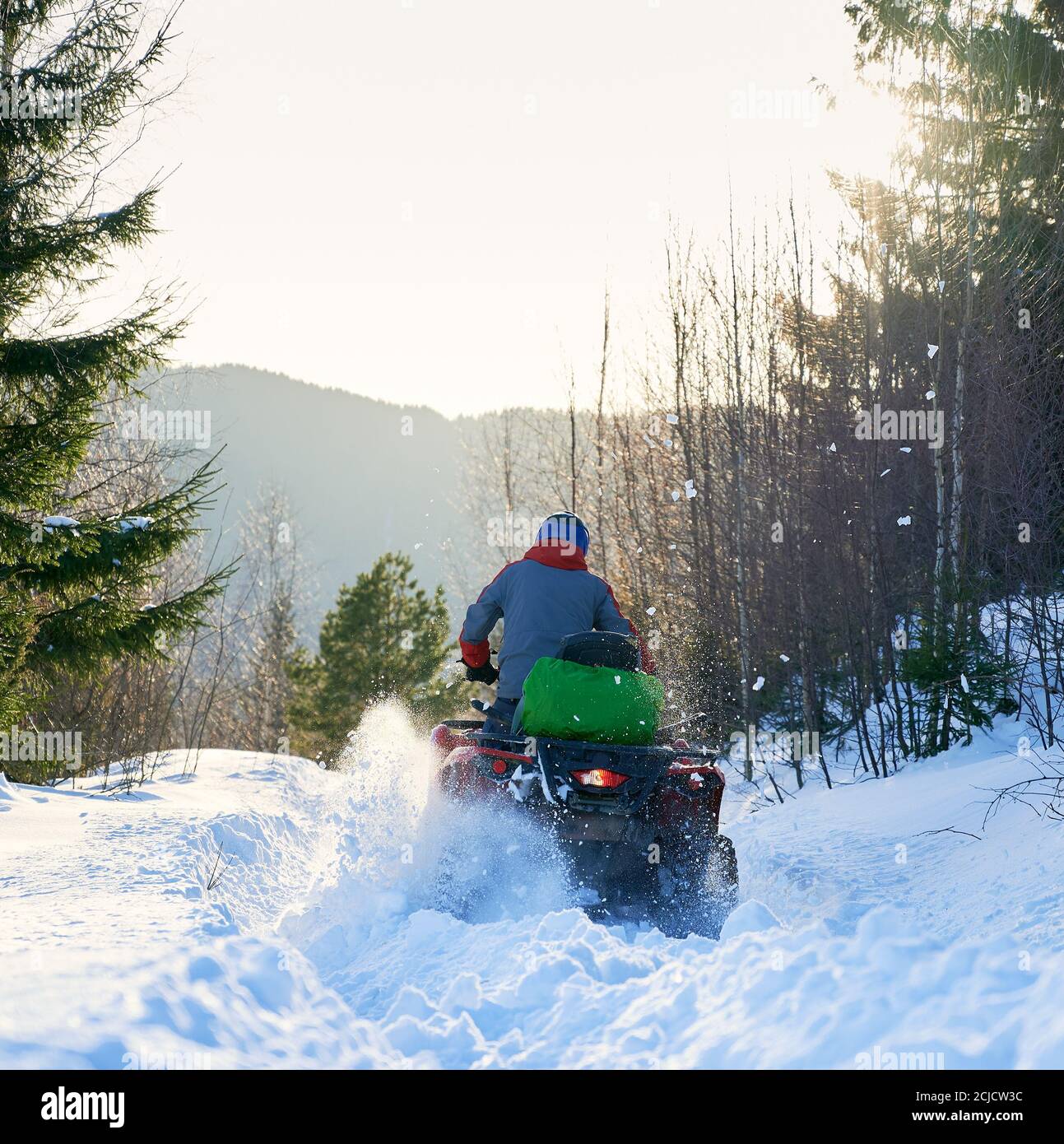 Rückansicht eines Bikers, der im Winter in den Bergen mit dem Vierrad-ATV fährt. Offroad-Fahrt im Schnee im Wald, hellen sonnigen Tag. Konzept des Wintersports Stockfoto