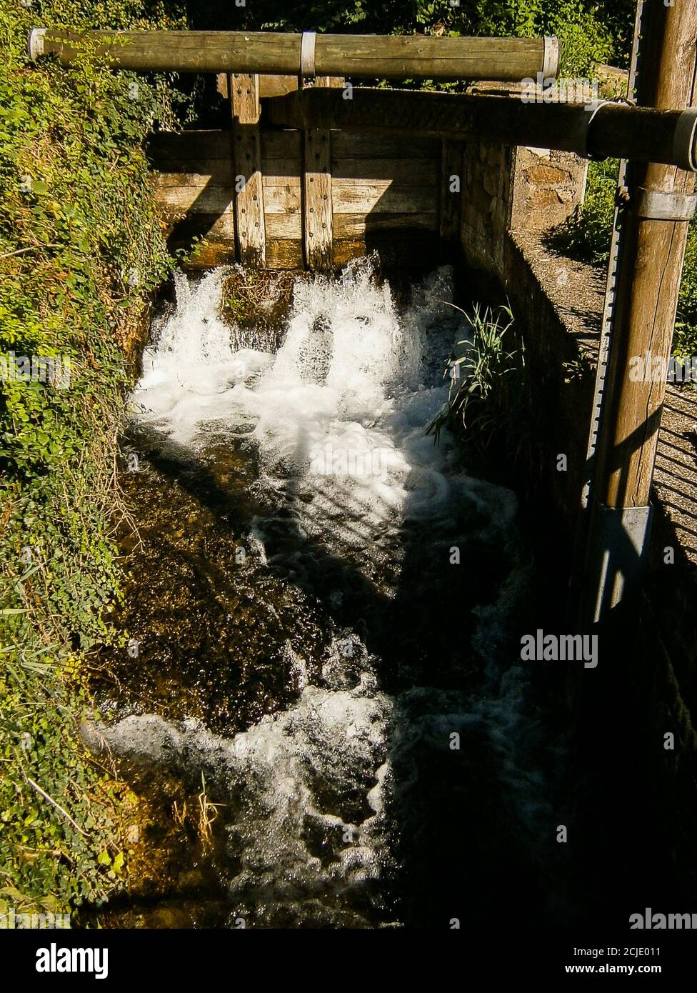 Ein Mühlbach mit einer alten Schleuse. Ihr könnt sehen, wie das Wasser durch sie fließt. Stockfoto