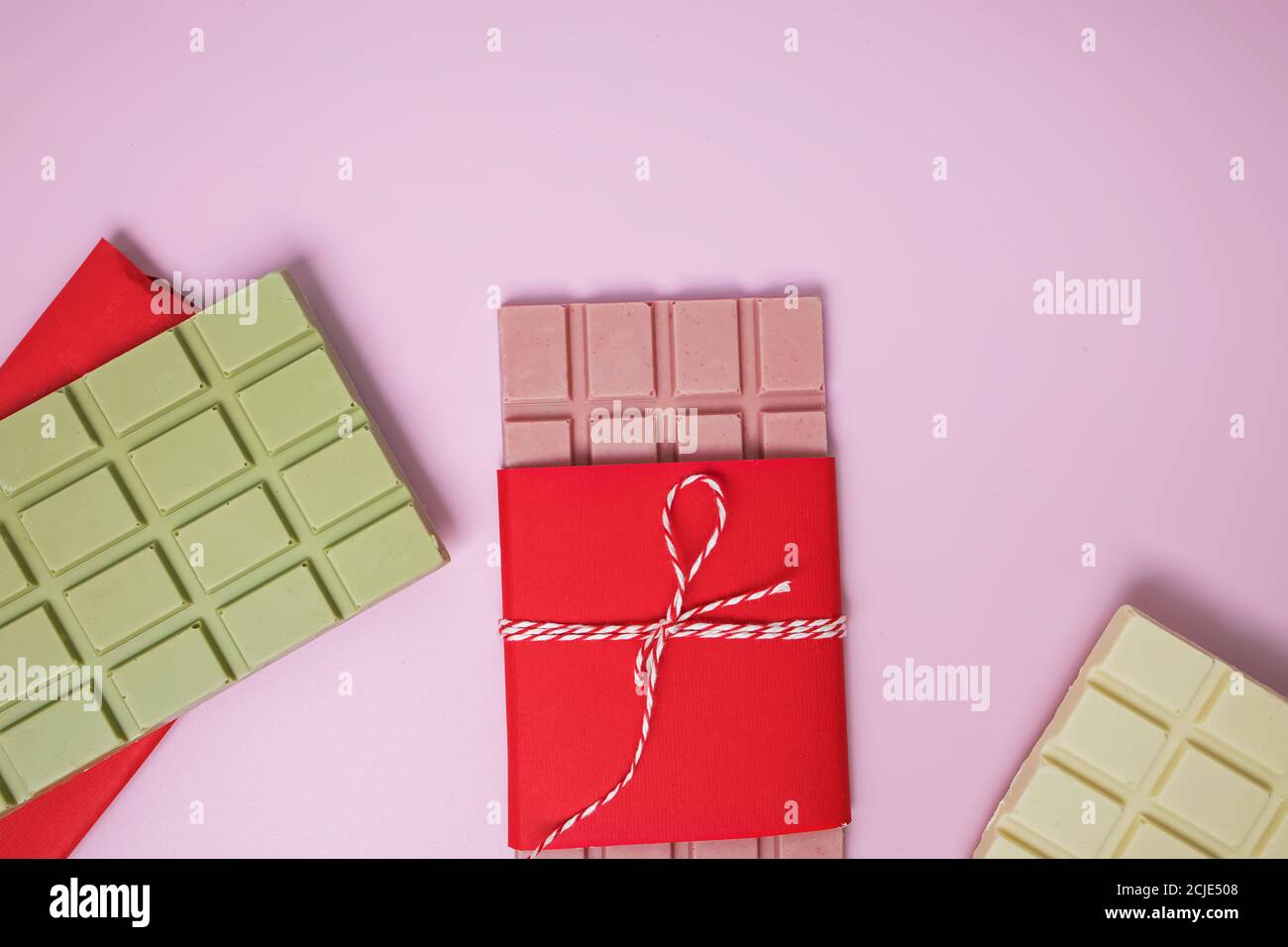 Schokoladenriegel mit verschiedenen Geschmacksrichtungen: Erdbeere, Matcha, Vanille. Grüne, weiße und rosa Schokolade auf rosa Hintergrund. Stockfoto