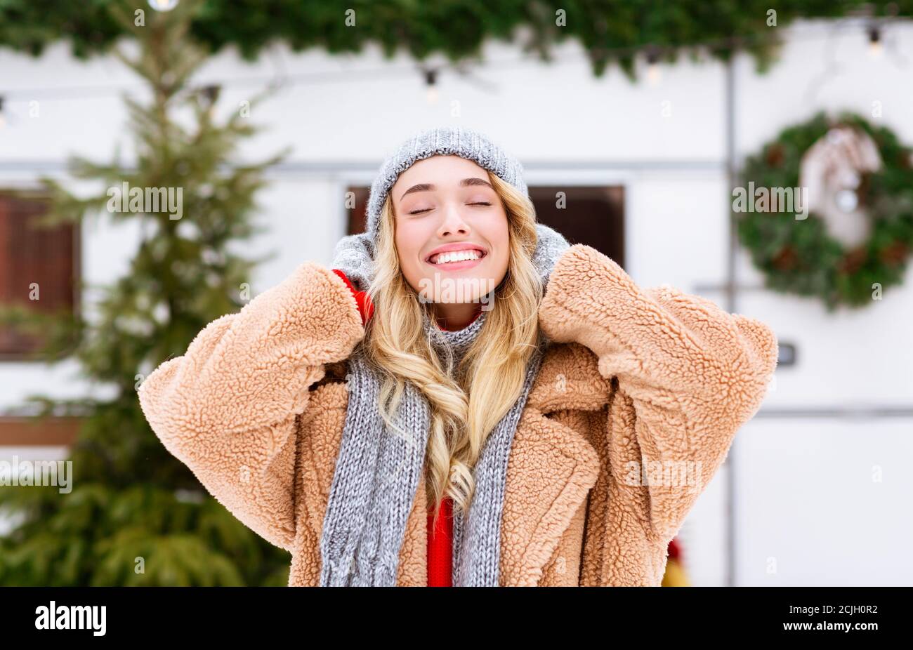 Lächelndes blondes Mädchen in gestricktem Hut genießen verschneiten Morgen an Wintercampingplatz Stockfoto