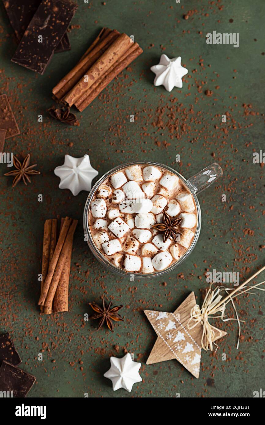Glas Tasse heiße Schokolade oder Kakao mit Marshmallows und Anis, Stücke von Schokolade, Meringue und Gewürze auf grünem Hintergrund. Traditionelle Winter drin Stockfoto