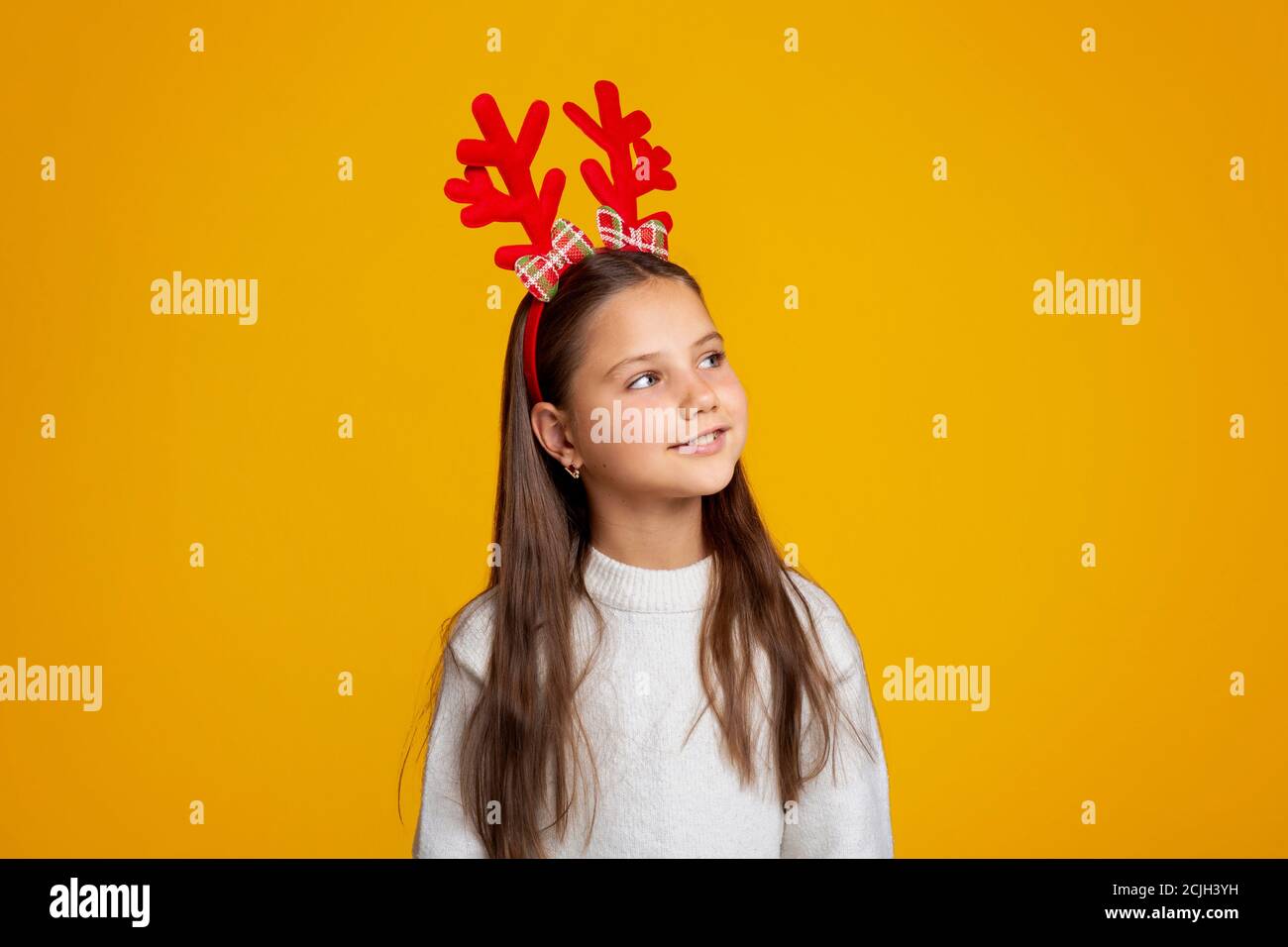 Kind wartet auf den Weihnachtsmann. Schöne kleine Mädchen mit Hörnern in Pullover schaut auf leeren Raum Stockfoto