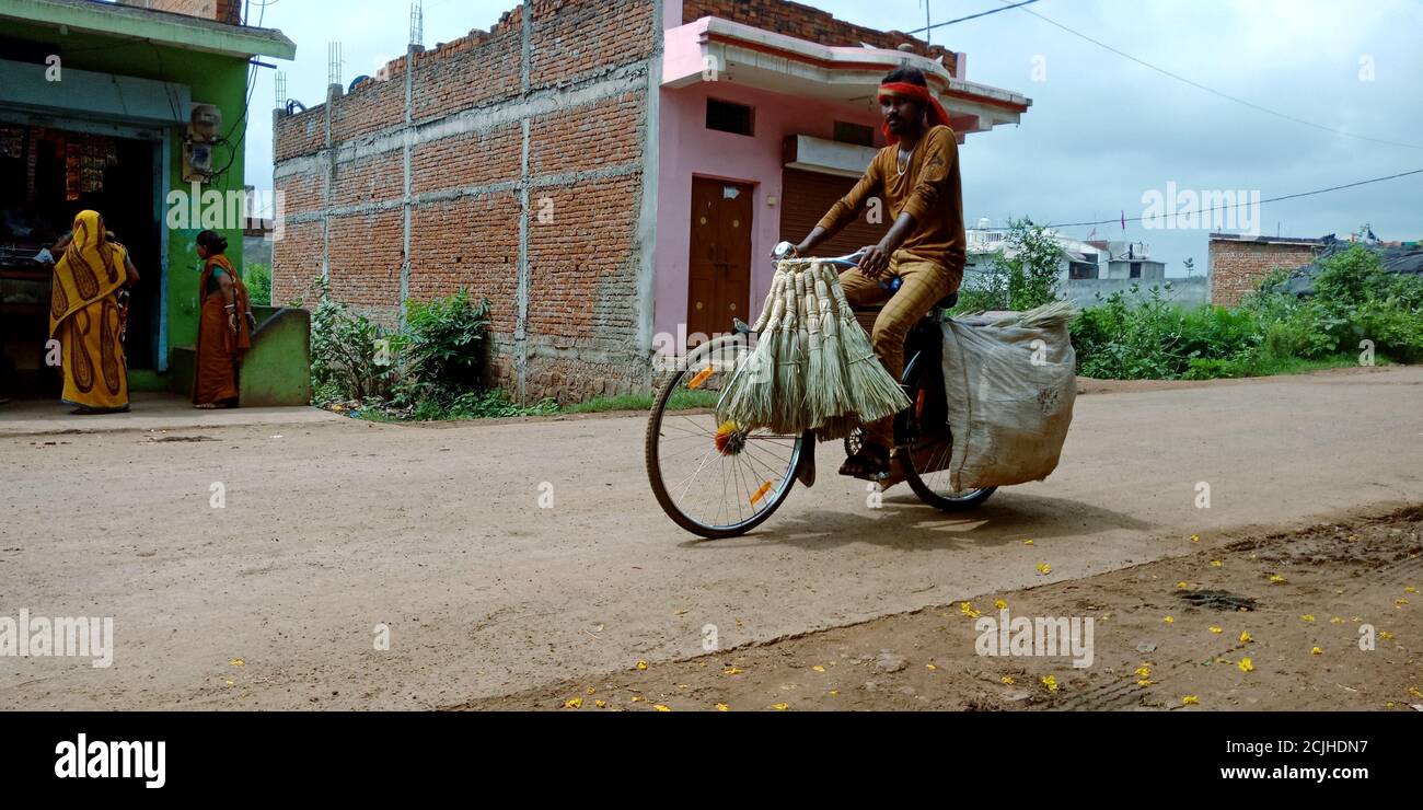 DISTRIKT KATNI, INDIEN - 03. SEPTEMBER 2019: Ein indischer Straßenvender, der Besen am Fahrrad auf der Straße im Dorf außerhalb des Marktes verkauft. Stockfoto