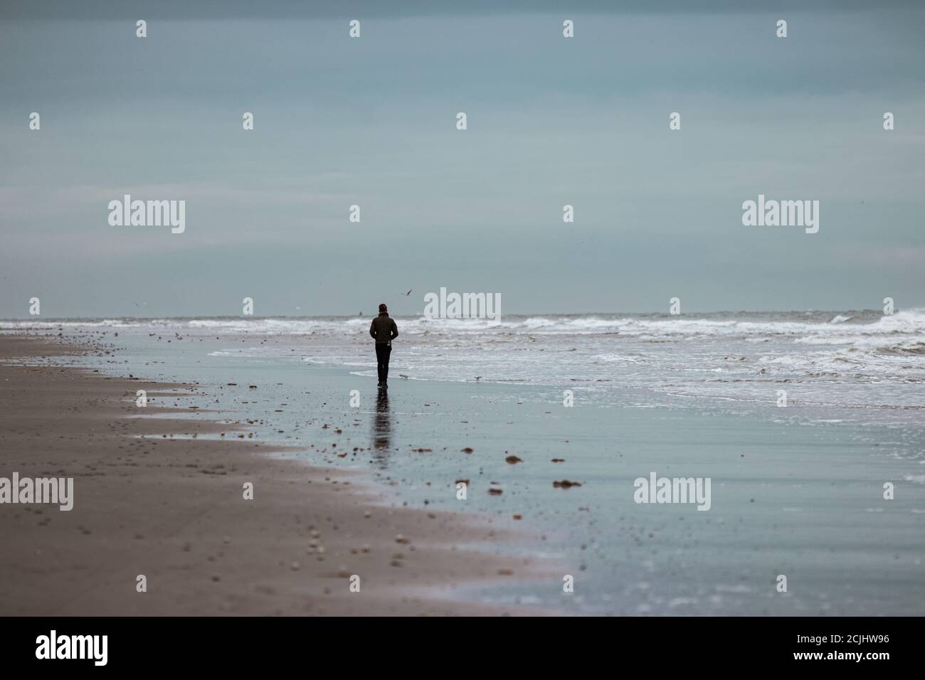 Mann, der alleine an einem trostlosen Strand läuft. Stockfoto