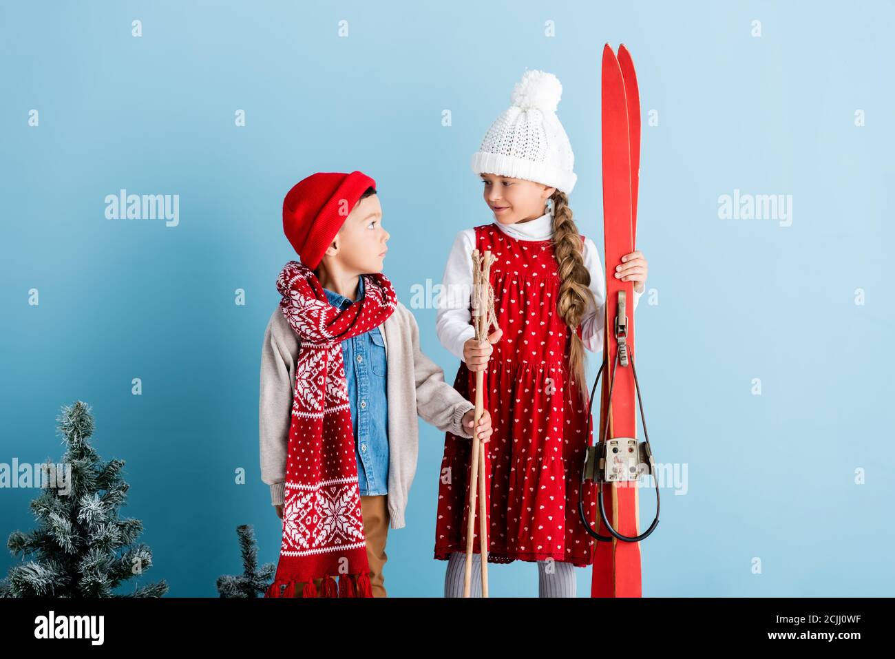 Mädchen im Hut Blick auf junge, während Skistöcke halten Und Ski auf blau Stockfoto