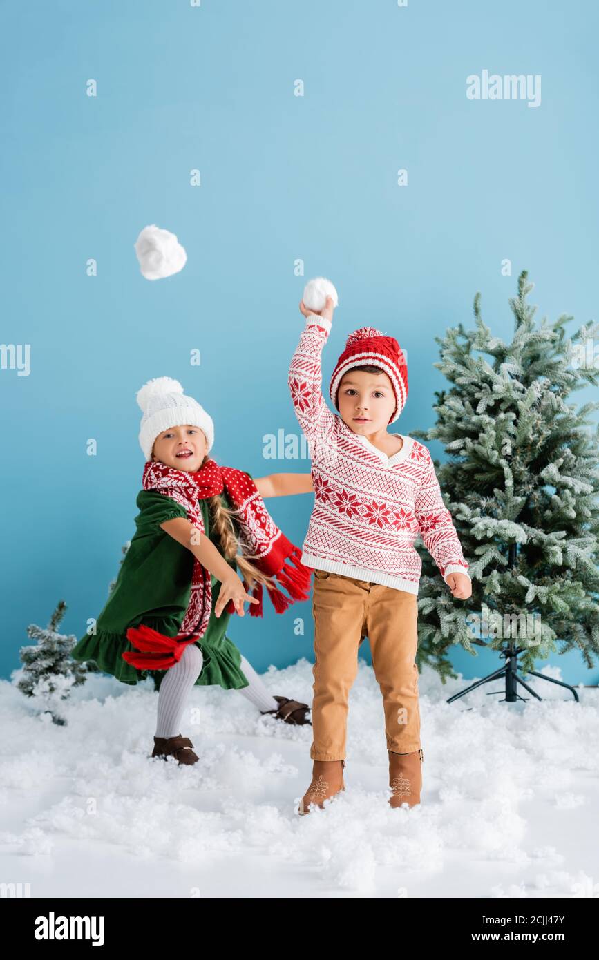 Kinder im Winter Outfit spielen Schneebälle in der Nähe von weihnachtsbäumen auf Blau Stockfoto