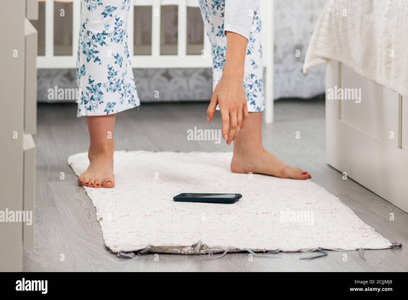 Die Frau beugt sich mit der Hand, um das Telefon, das auf den Boden gefallen ist, abzuheben. Nahaufnahme der Beine. Zuhause Bleiben Sie im Hintergrund. Das Konzept der los Stockfoto