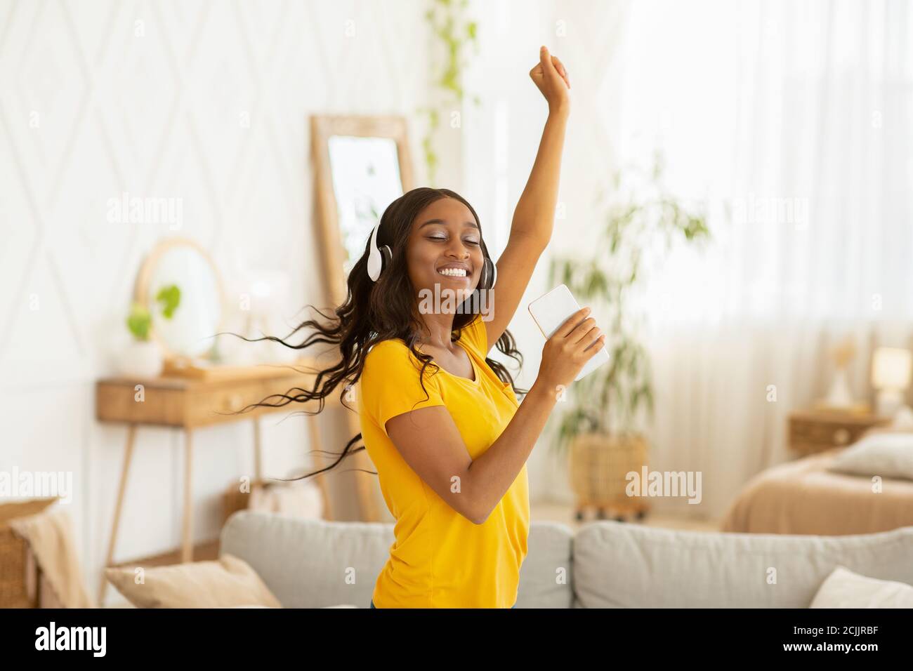 Glückliche junge schwarze Frau mit Kopfhörern und mobilen Gerät tanzen Zu ihrer Lieblingsmusik zu Hause Stockfoto