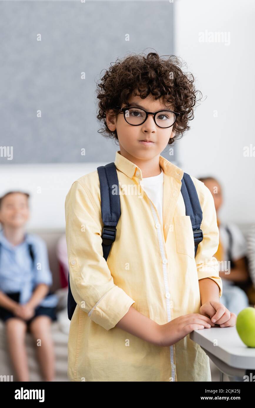 Selektiver Fokus des muslimischen Schuljungen mit Rucksack in der Nähe von Apfel stehen Auf dem Schreibtisch im Klassenzimmer Stockfoto