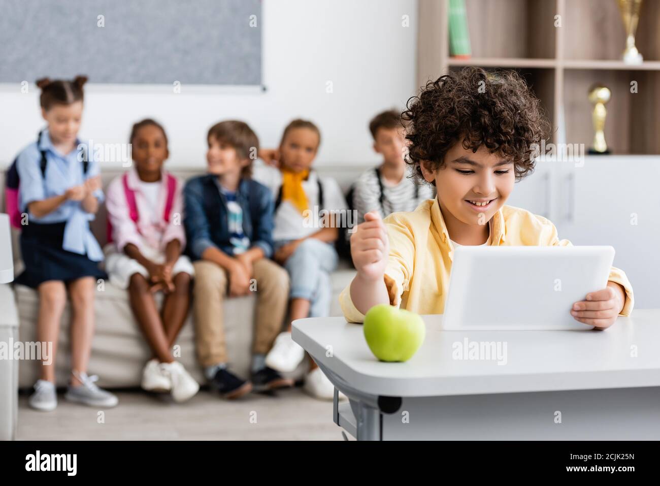 Selektiver Fokus des muslimischen Schuljungen mit digitalen Tablet in der Nähe von Apfel Auf dem Schreibtisch im Klassenzimmer Stockfoto