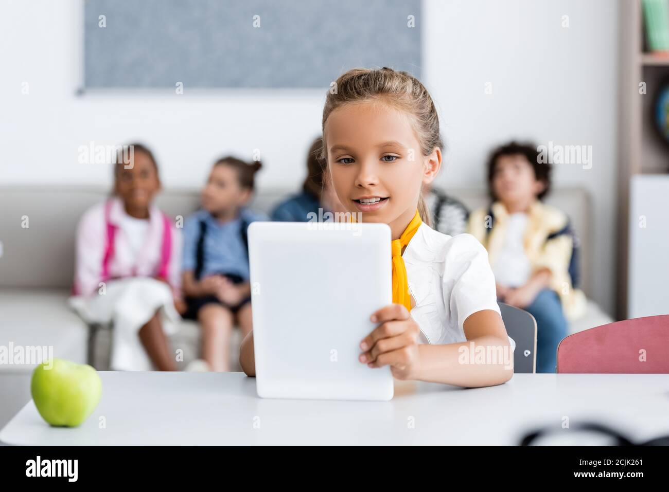 Selektive Fokus der Schülerin mit digitalen Tablet in der Nähe von Apfel und Multikulturelle Freunde im Klassenzimmer Stockfoto