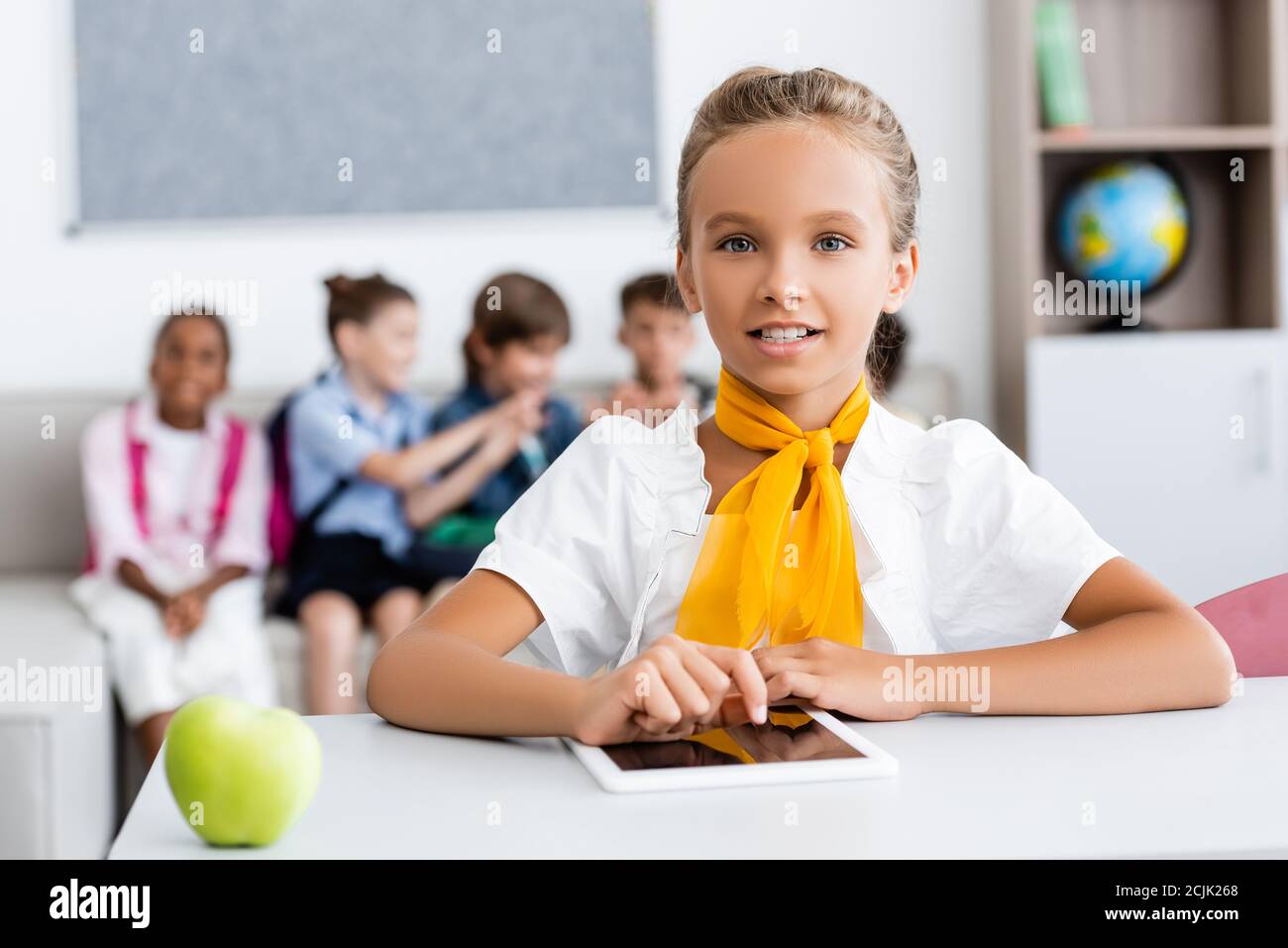 Selektive Fokus der Schülerin mit digitalen Tablet in der Nähe von Apfel und Multikulturelle Klassenkameraden im Klassenzimmer Stockfoto