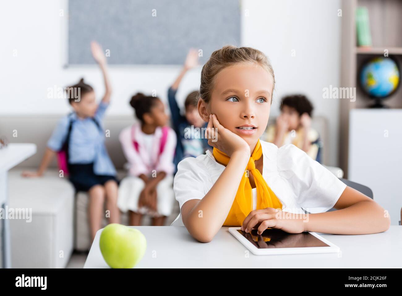 Selektive Fokus von Schulmädchen suchen weg in der Nähe von digitalen Tablet und apple auf dem Schreibtisch im Klassenzimmer Stockfoto