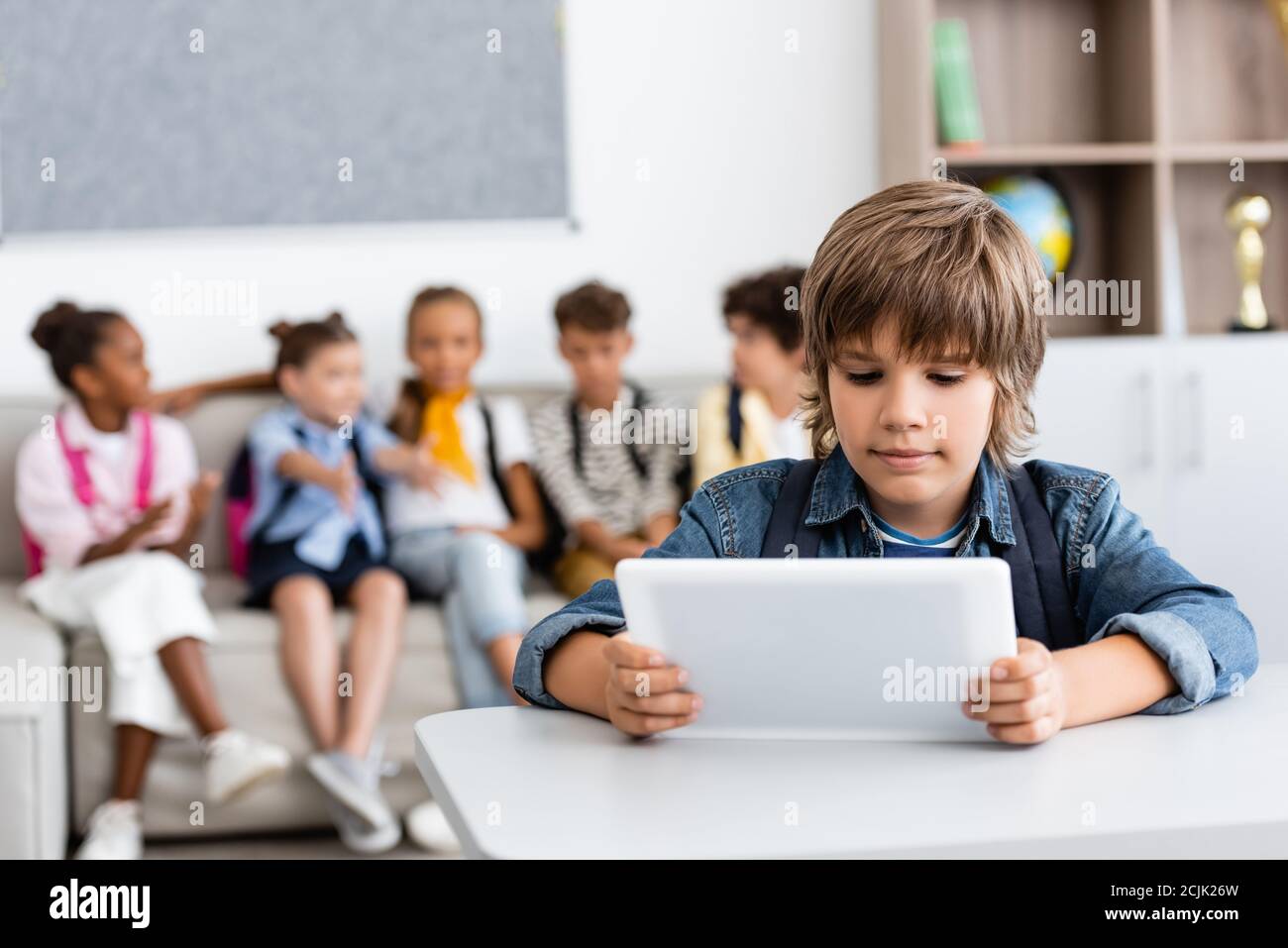 Selektiver Fokus des Schuljungen halten digitale Tablet am Schreibtisch mit Multikulturelle Freunde im Hintergrund Stockfoto