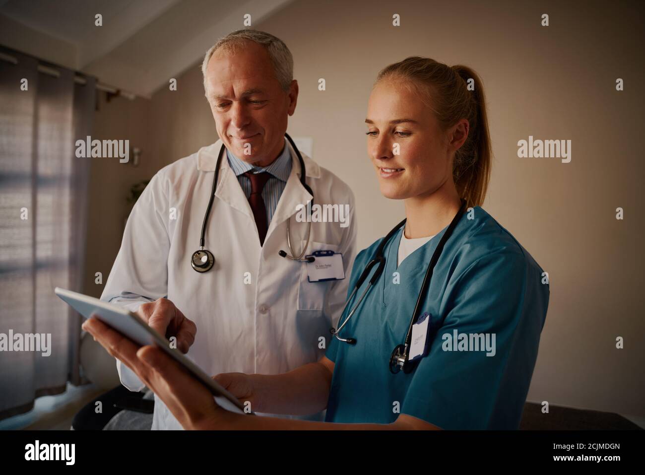 Junge Krankenschwester im Gespräch mit älteren männlichen Arzt diskutieren Medizinische Berichte auf digitalen Tablet im Krankenhaus Stockfoto