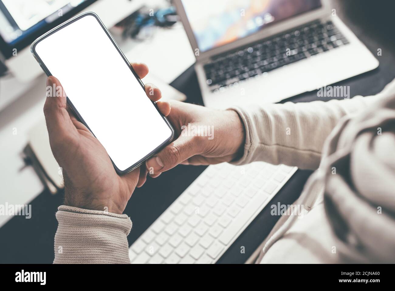 Über die Schulter Blick der Person hält Smartphone mit blank Weißer Touchscreen am Schreibtisch Stockfoto