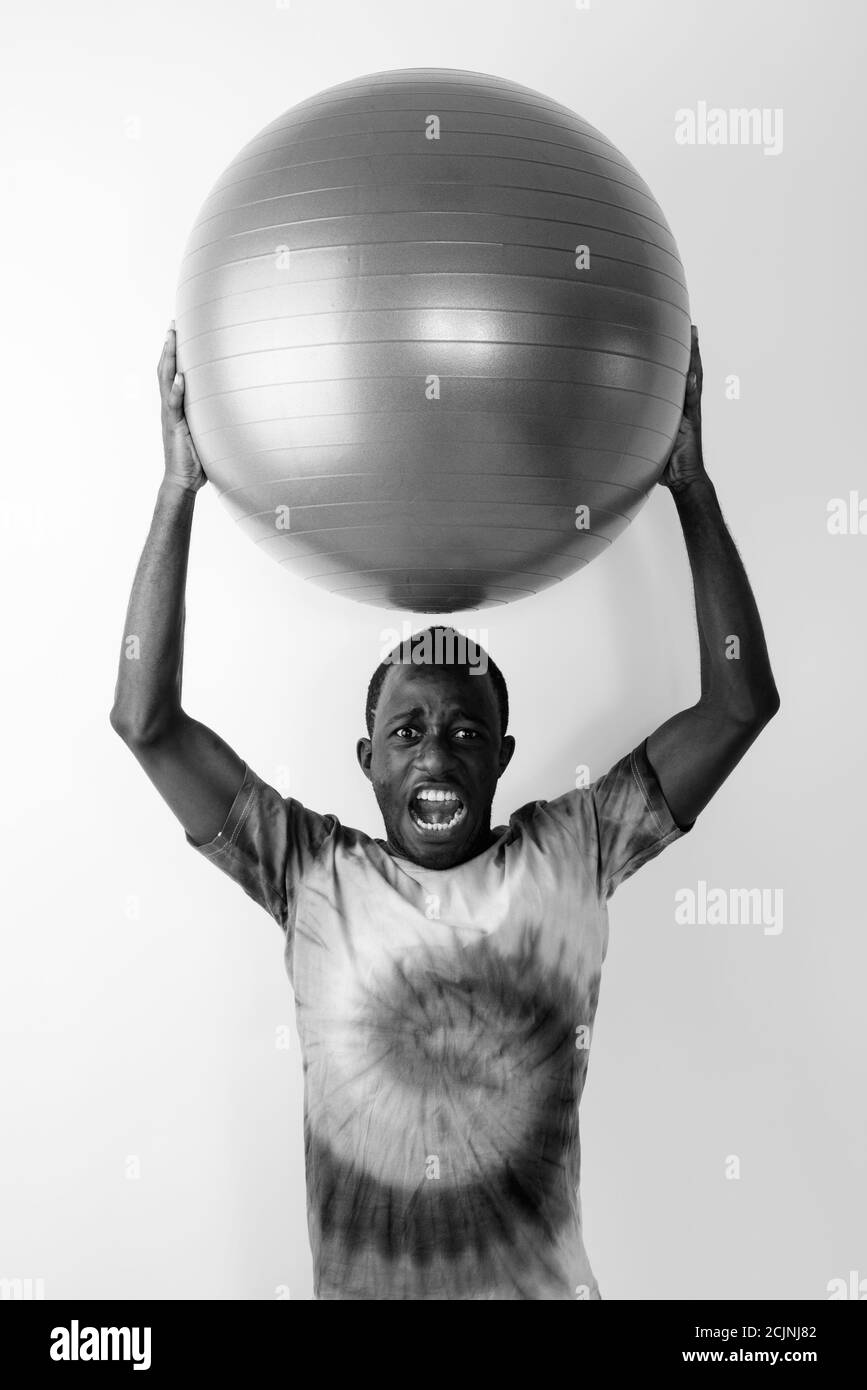 Studioaufnahme eines jungen schwarzen afrikanischen Mannes, der große Übung hält Ball auf dem Kopf bereit für die Turnhalle gegen Weißer Hintergrund Stockfoto